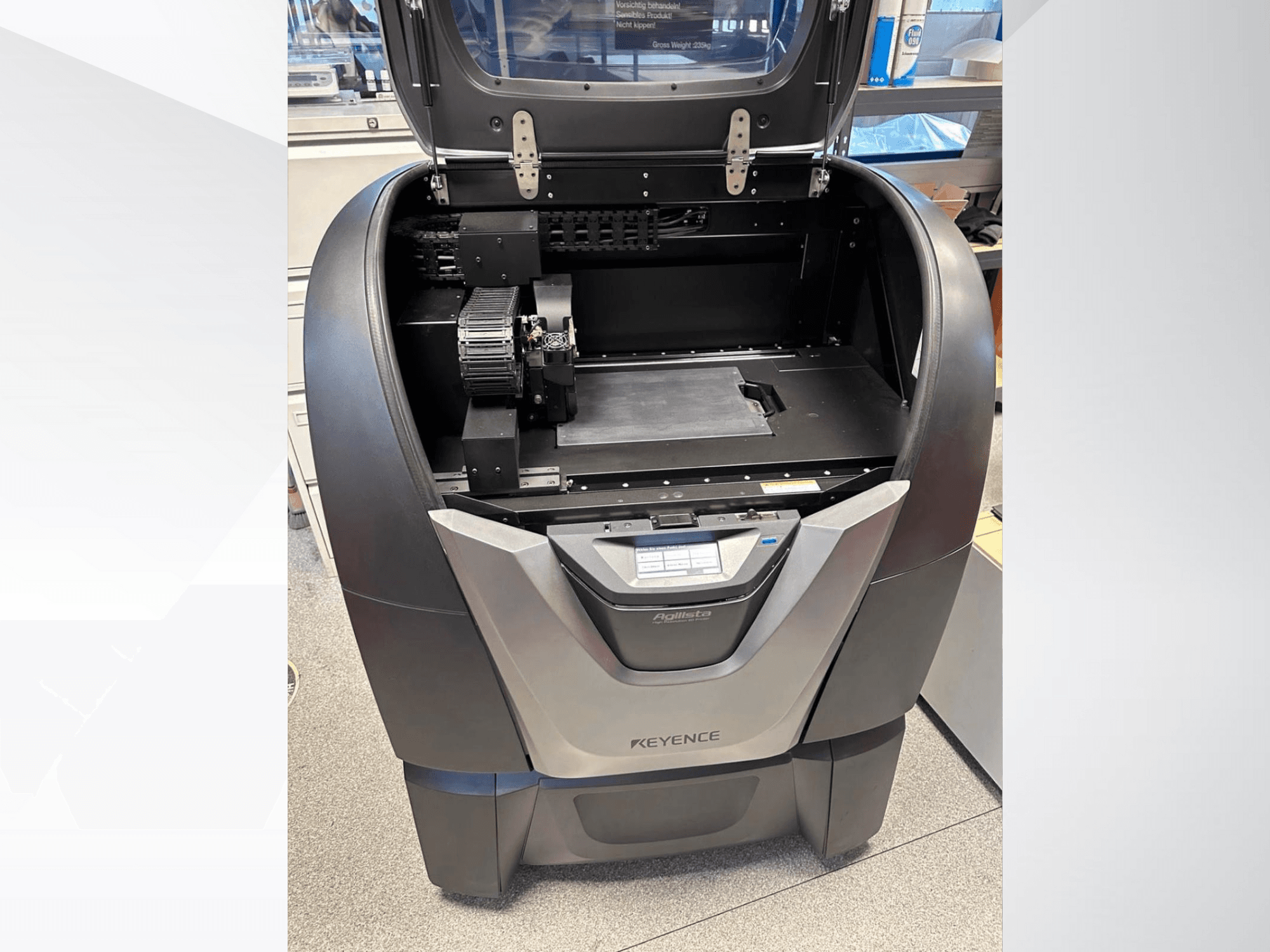 KEYENCE Agilista 3D-skrivare, framifrån, visar den öppna ovansidan, den stora byggplattformen och de interna mekaniska komponenterna.