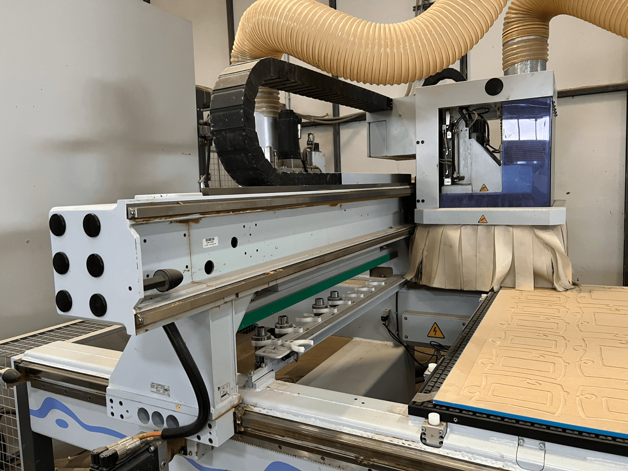 Sidovy av en CNC-fräs med blå och silverfärgad kontrollpanel, utrustad med dammutsug och en bädd för träkapning.