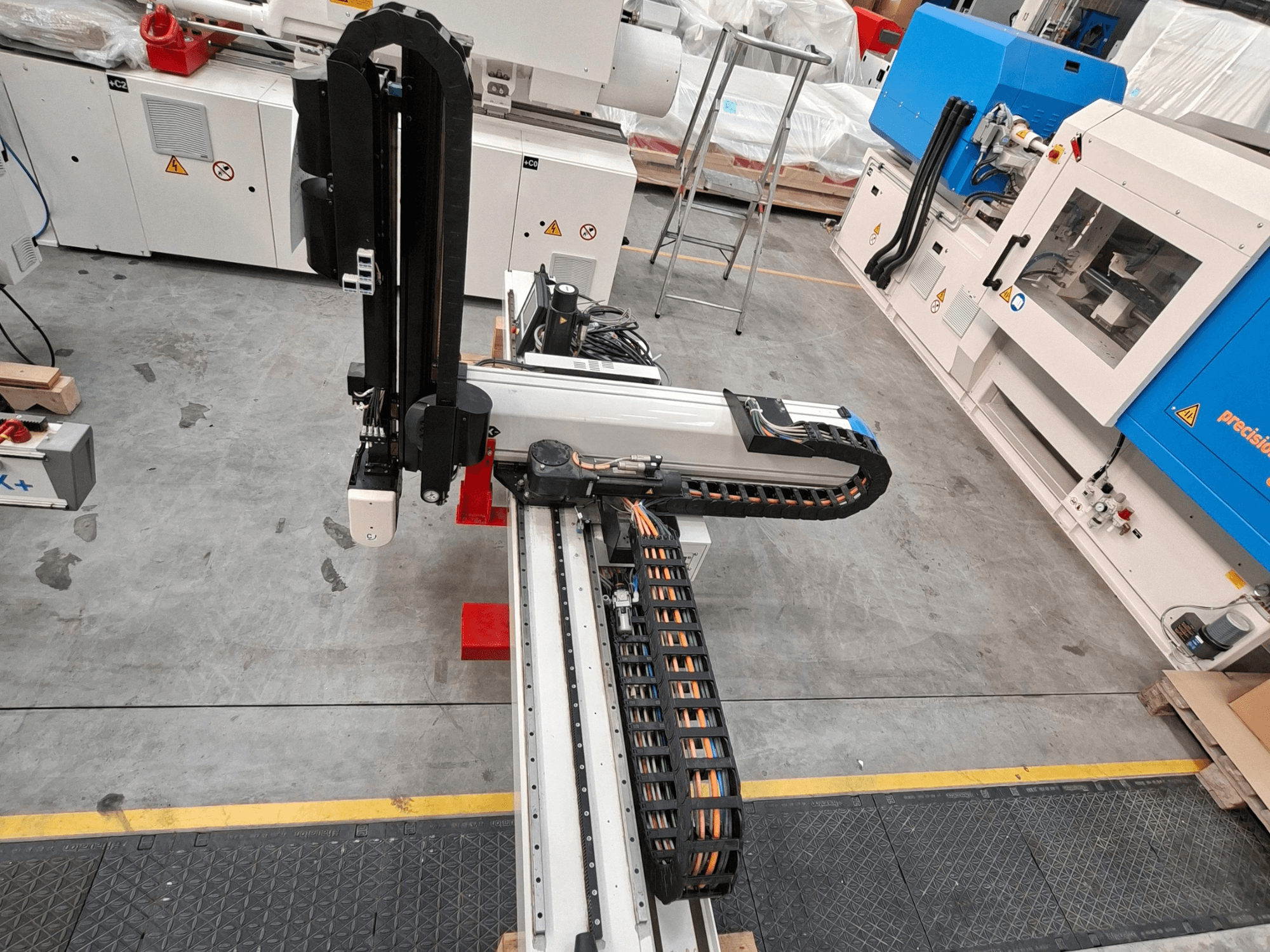 Plastbearbetningsmaskinen Krauss Maffei LRX150-MC5 sett ovanifrån, där robotarmen och kabelkanalen på fabriksgolvet syns tydligt.