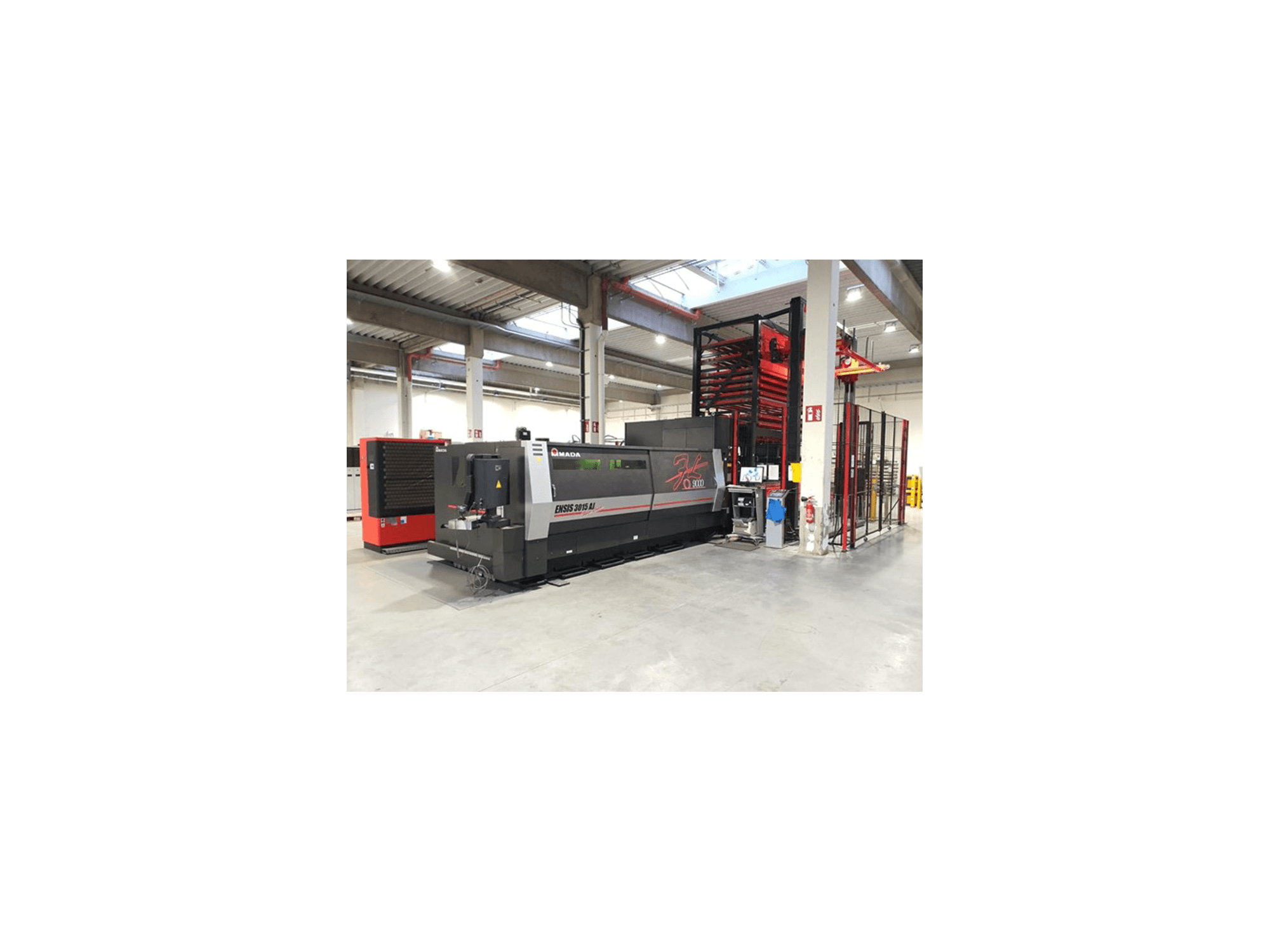 Amada ENSIS 3015 Aj laserskärmaskin framifrån, placerad i en rymlig industriell verkstad med metallhyllor.
