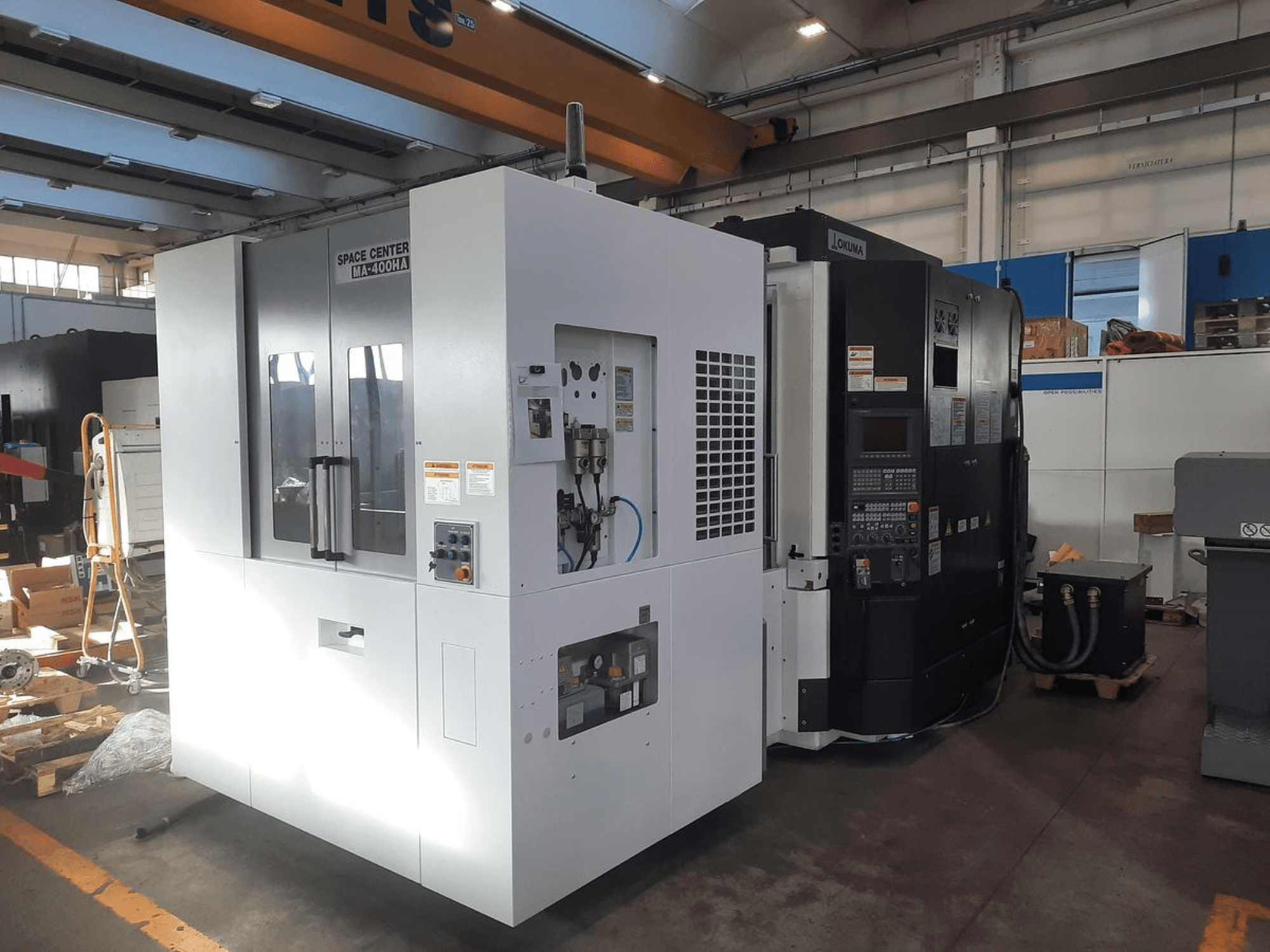 Frontvy av CNC-maskinerna IM-400HAA och OKUMA från SPACE CENTER med olika reglage och tillverkaretiketter.