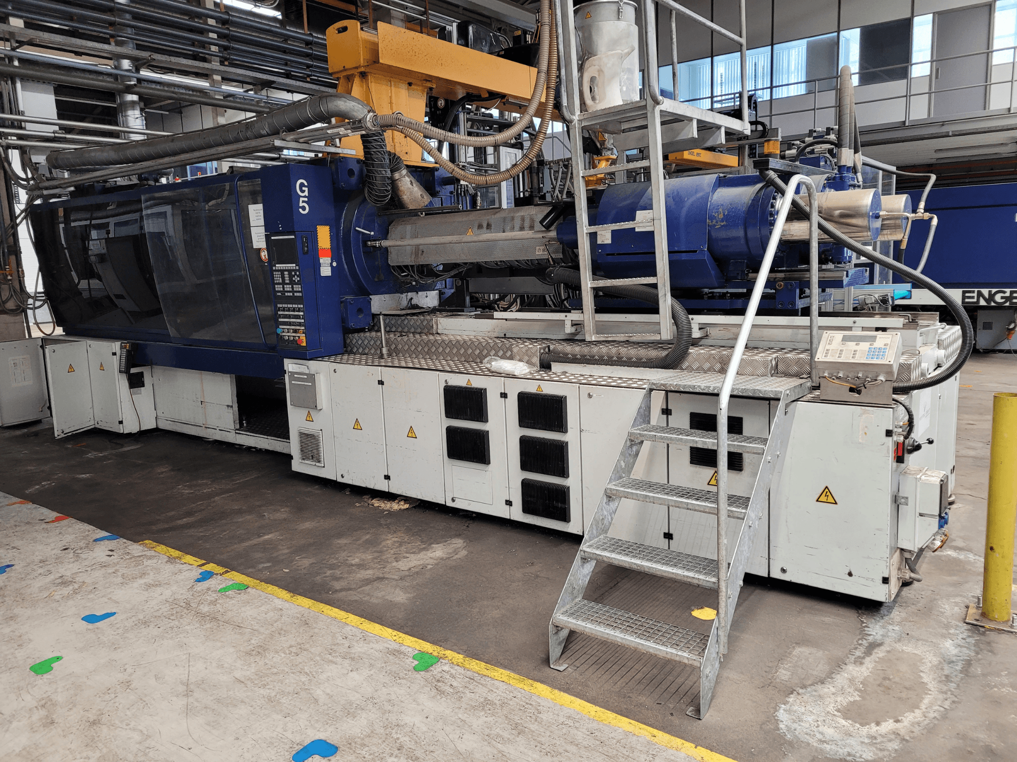 Formsprutningsmaskin G5, vy från sidan, med kontrollpanel, trappstege och arbetsyta i rostfritt stål synliga.