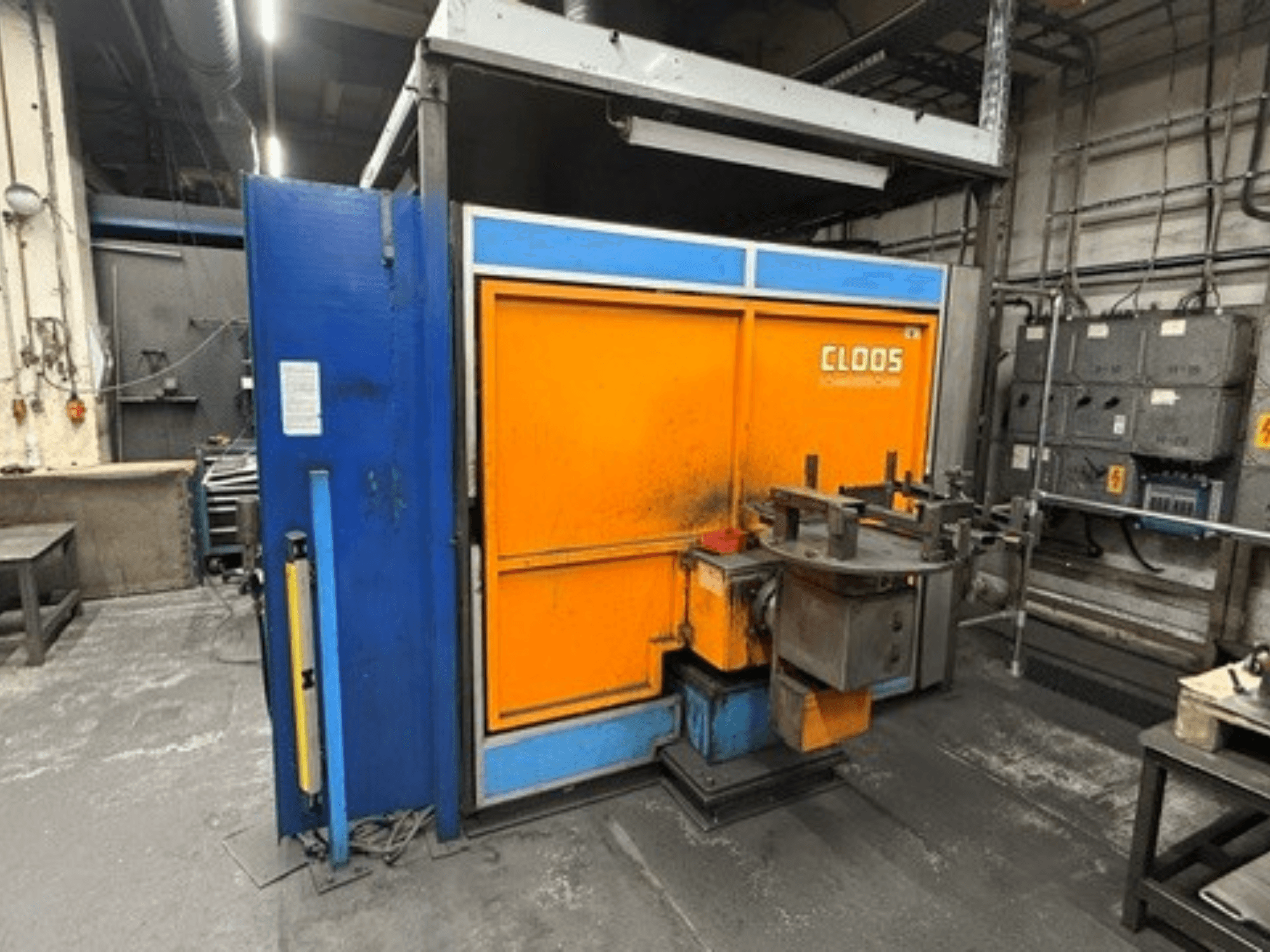 CLOOS Romat 320-svetsrobot i en verkstad, framifrån sett, med orange och blå hölje samt kontrollpanel och verktyg.