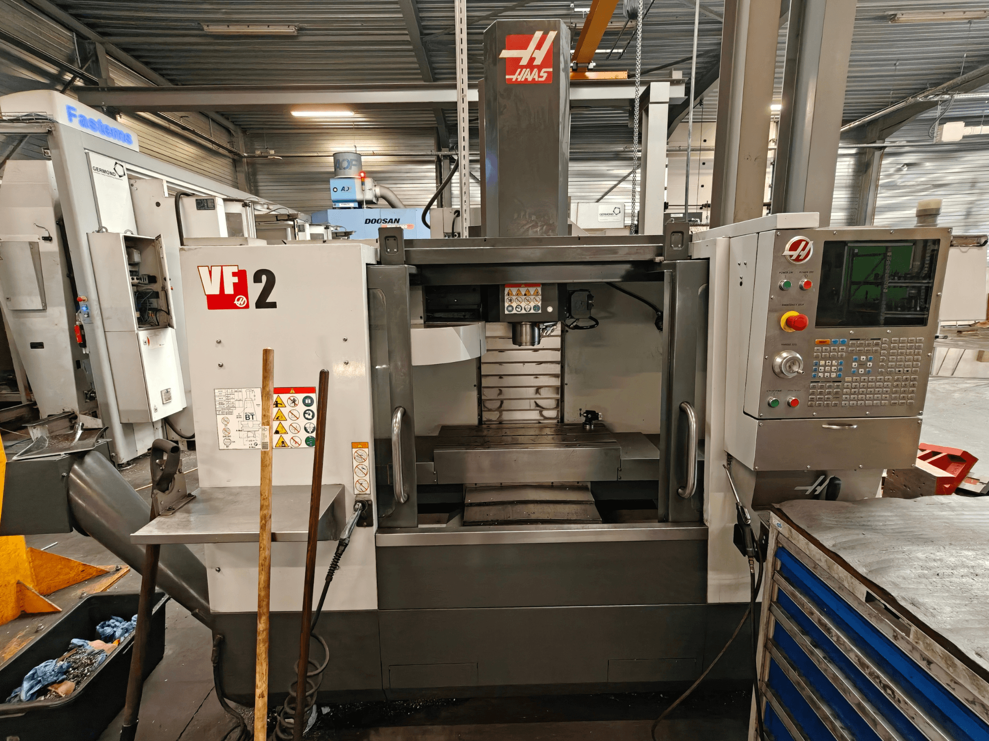 HAAS VF-2 vertikalt bearbetningscenter, framifrån, där man ser manöverpanelen, spindeln och arbetsbordet i en verkstadsmiljö.