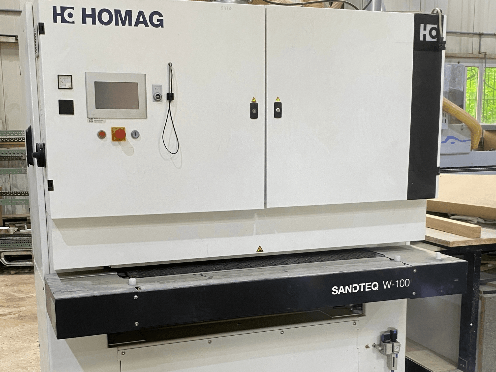 HOMAG SANDTEQ W-100 bandslipmaskin i en verkstad, där man ser kontrollpanelen, dammuttaget och slipbandsområdet. Framifrån.