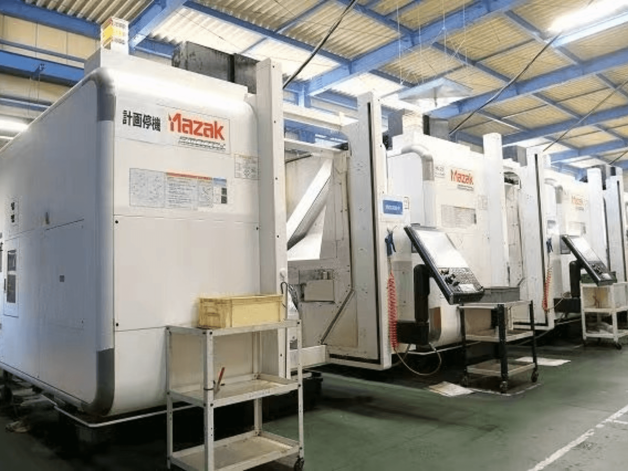 Mazak CNC-maskiner i en fabriksmiljö, sidovy som visar kontrollpaneler och etiketter på vita kroppar.