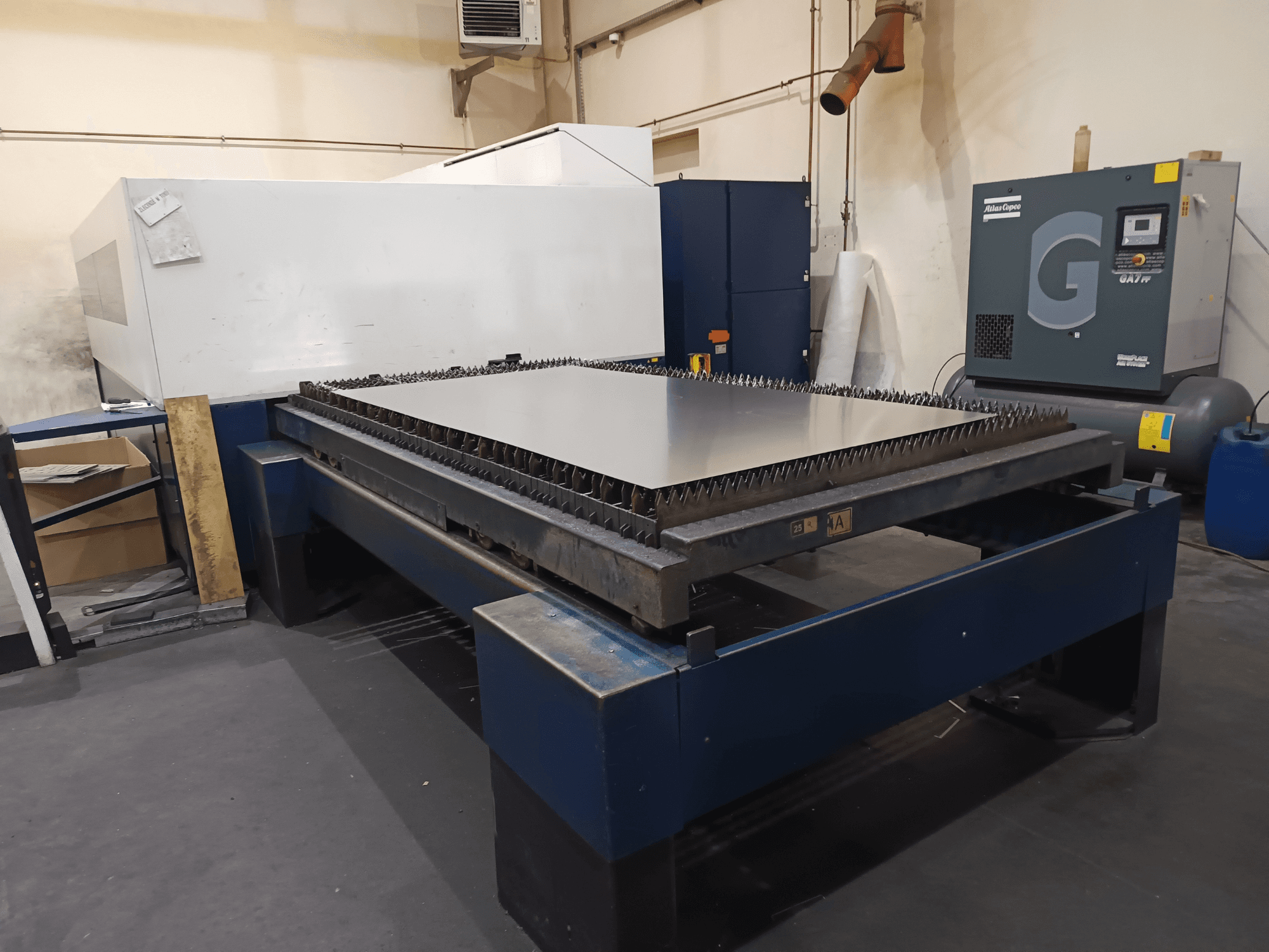 Industriell skärmaskin med metallbord, vy framifrån. Med vassa kanter, luftkompressor till höger och stålram.