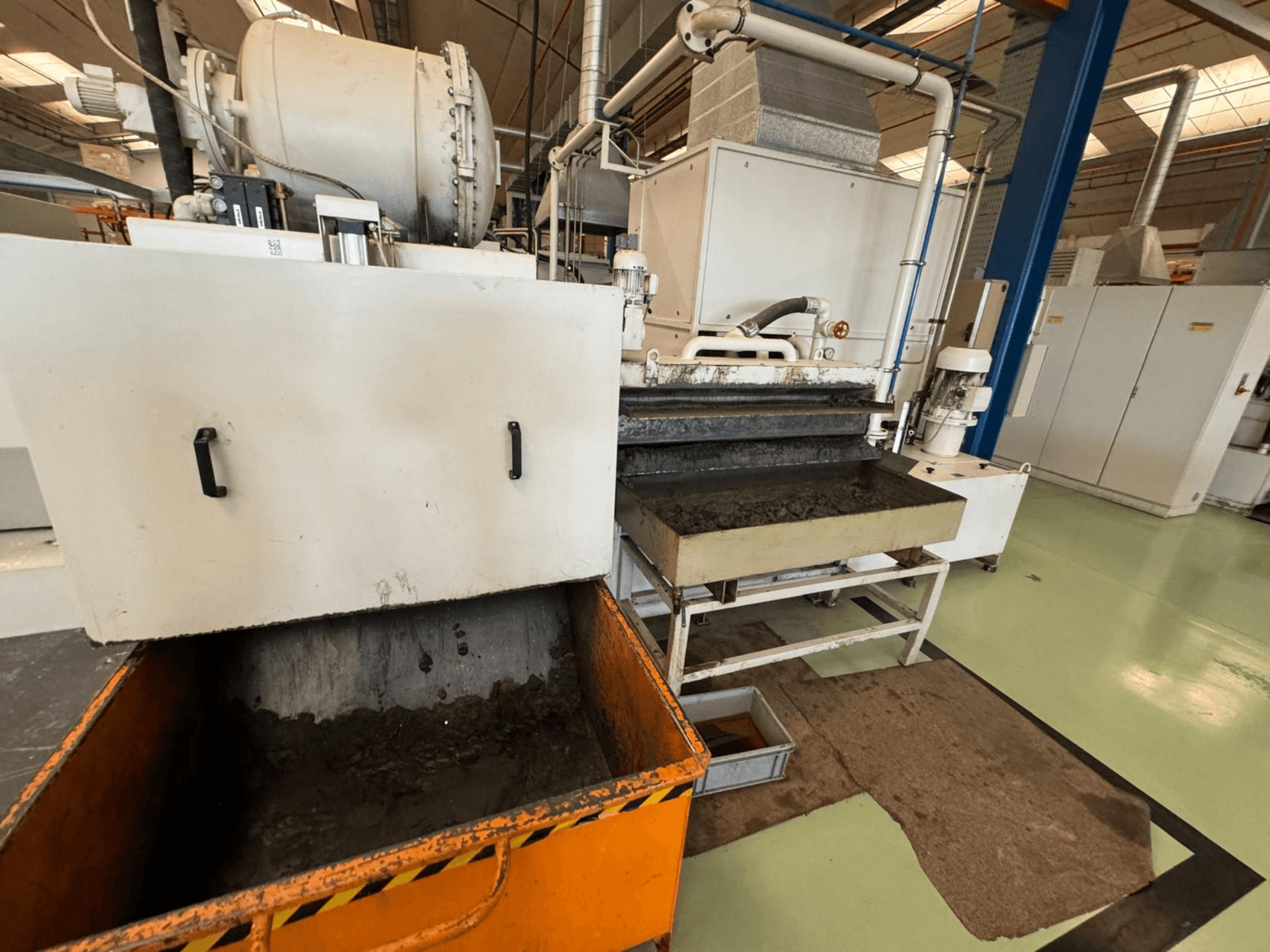 Industriell bearbetningsutrustning med en orange soptunna, framifrån; innehåller en motor, transportörer och underhållsområde.