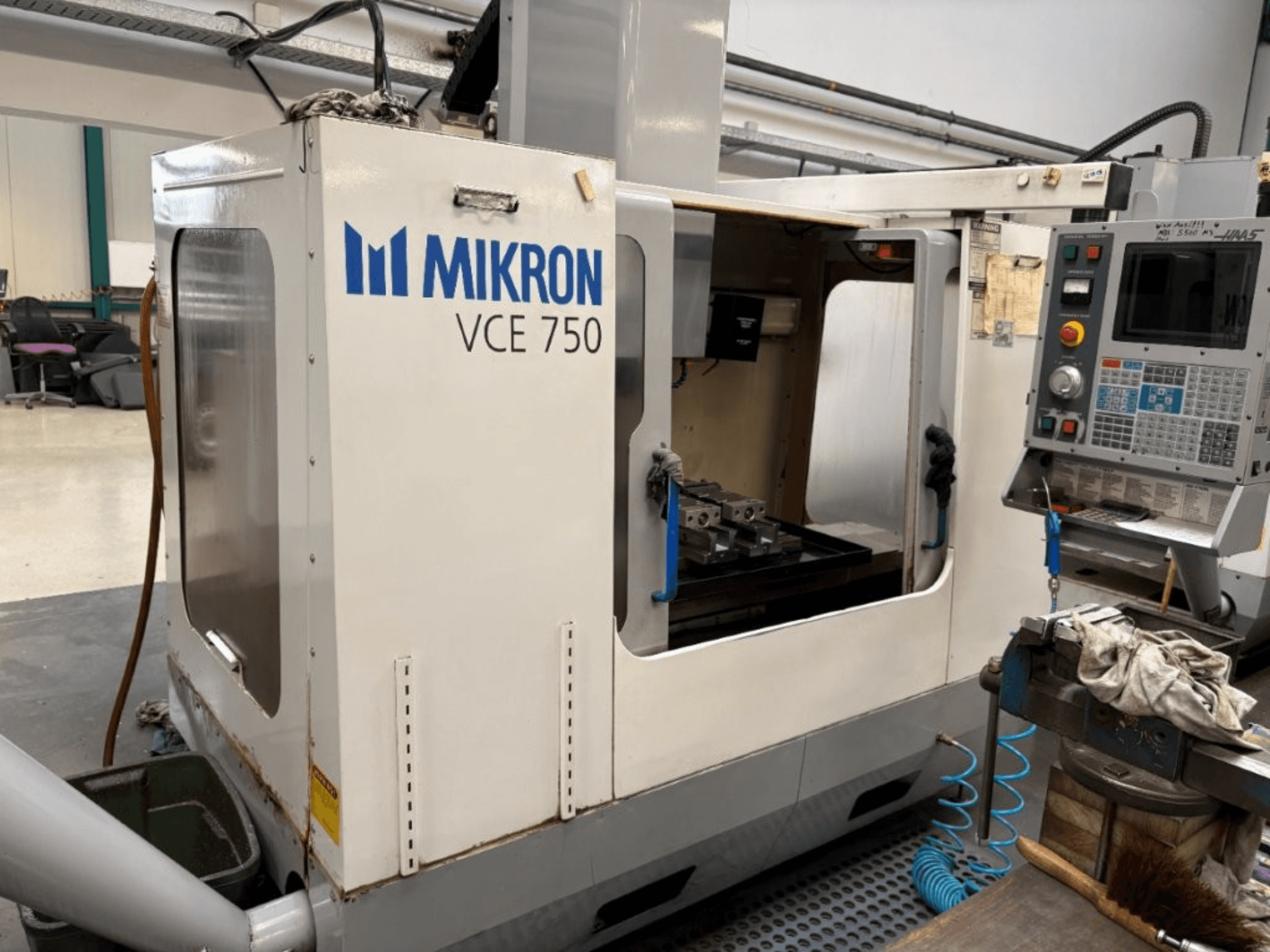 Mikron VCE 750 CNC-fräsmaskin framifrån, med maskinbearbetat arbetsbord och kontrollpanel med olika knappar och skärmar.