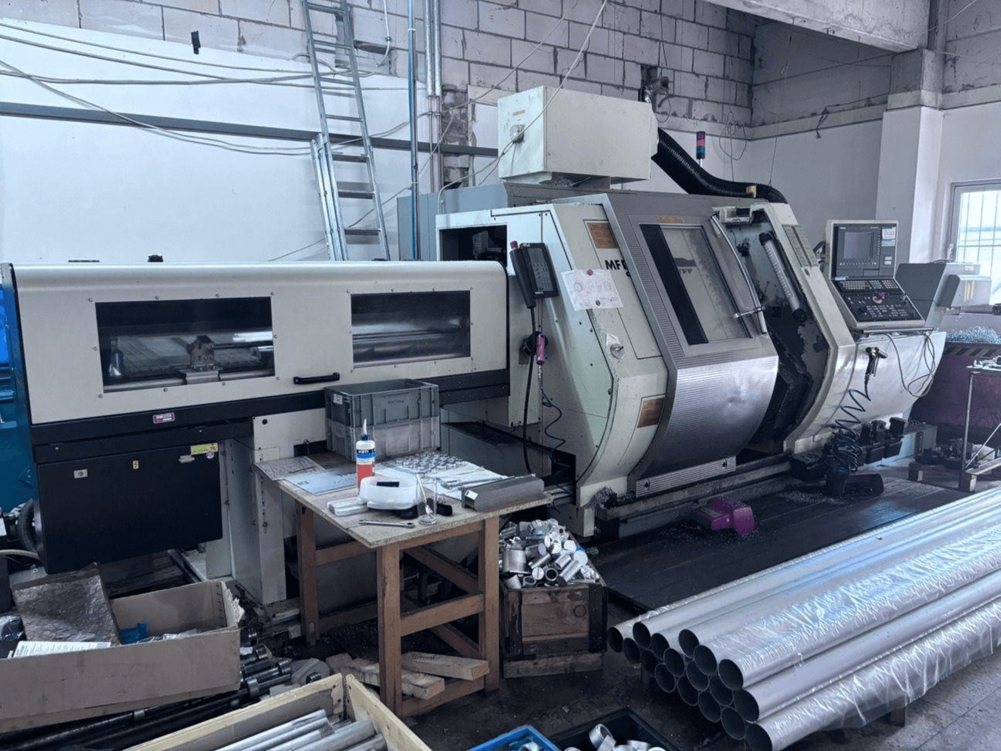 Gildemeister MF Twin 65 svarv-fräscenter, sidovy som visar kontrollpanelen, bearbetningsområdet och aluminiumrören.