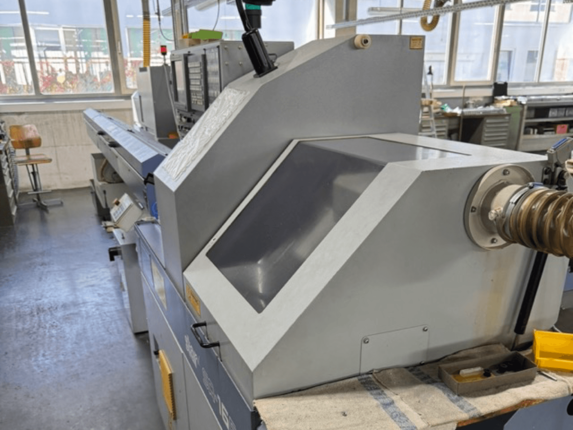 Grå industrimaskin sedd från sidan, har en stor vinklad panel, manöverknappar och slangfäste.