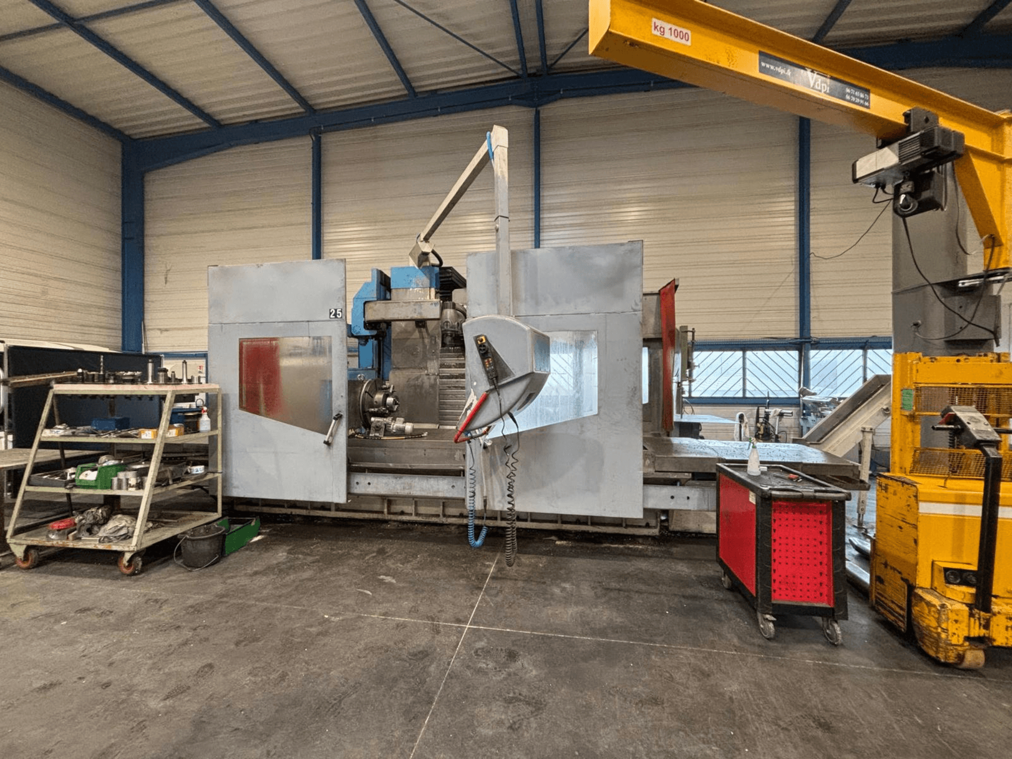 CNC-fräsmaskin från sidan i en verkstad; synliga verktyg och förvaringshyllor. Märke och modell ej specificerade.