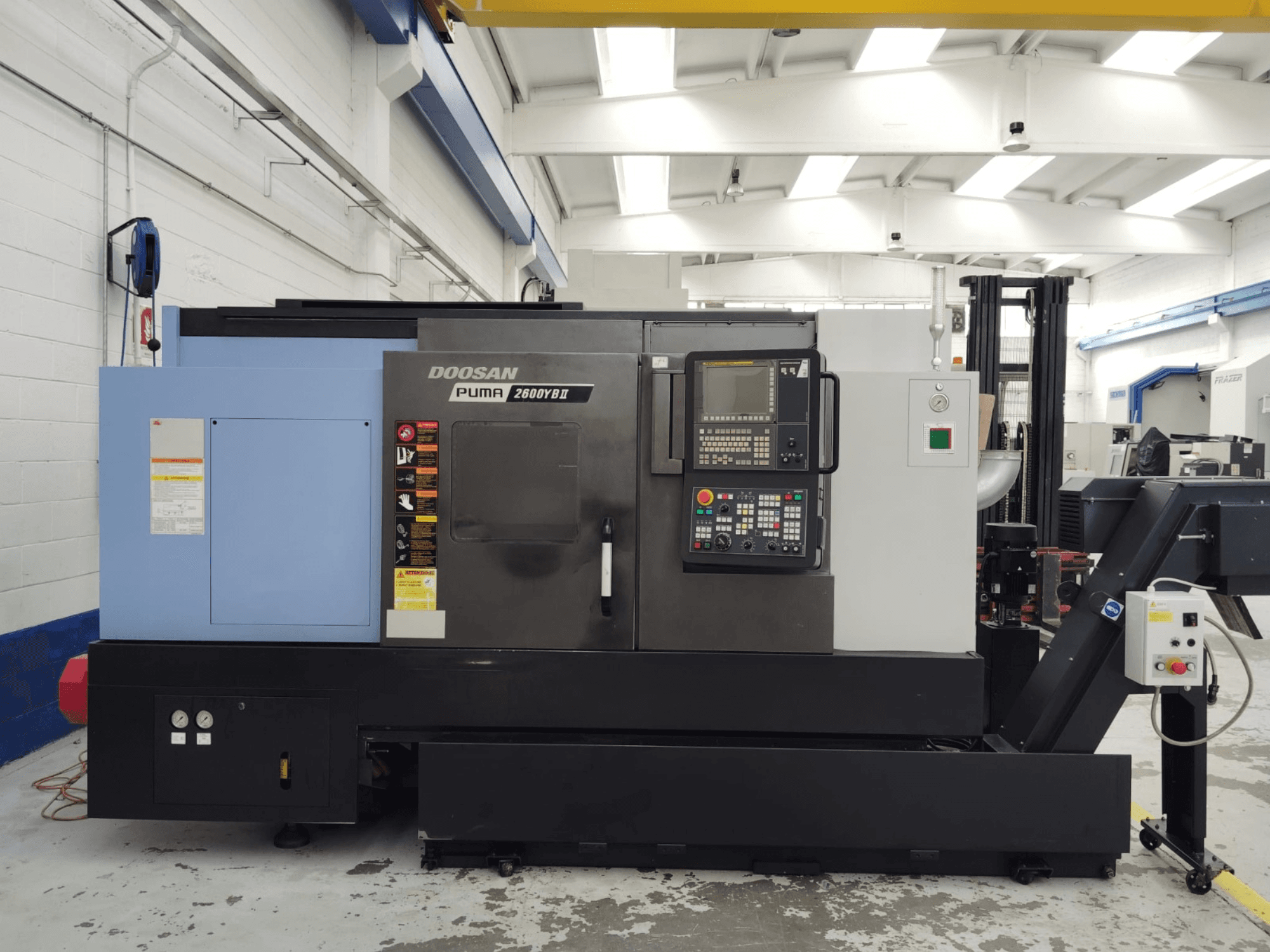 Frontvy av DOOSAN Puma 2600YB II horisontell svarv med kontrollpanel och säkerhetsetiketter synliga.