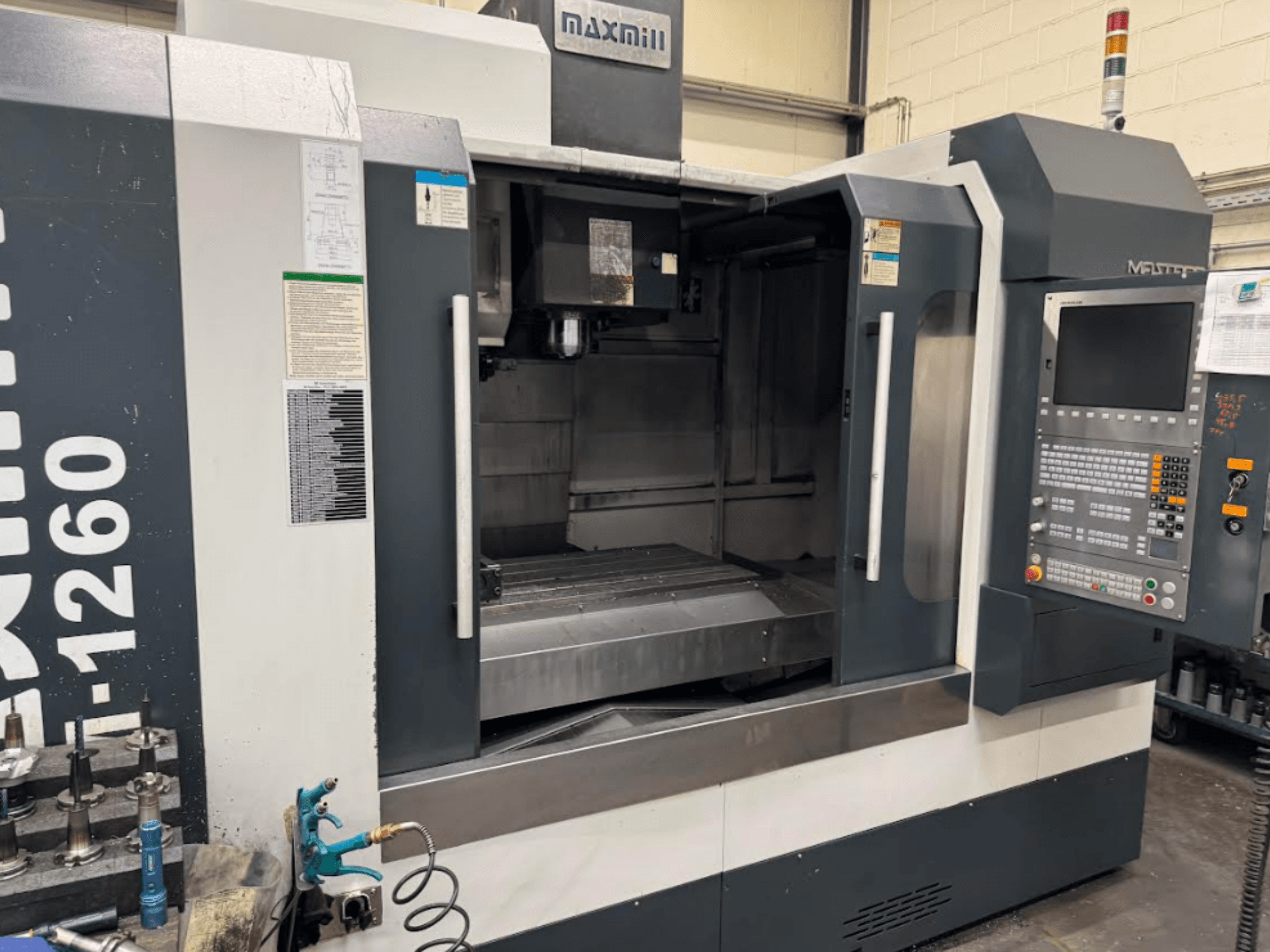 Maxmill CNC-fräsmaskin, modell M-1260, framifrån visar tom arbetsyta med kontrollpanel och bruksanvisning.