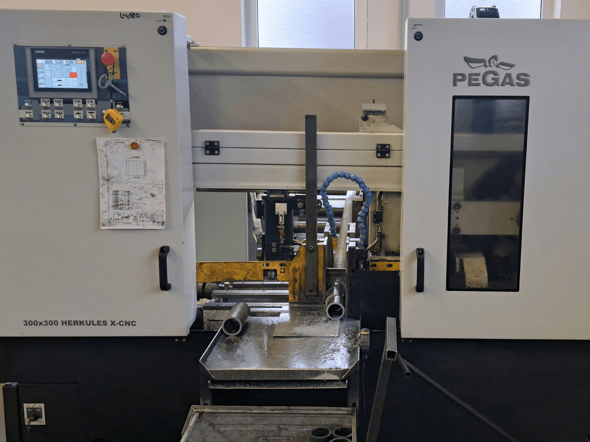 Pegas HERKULES X-CNC 300x300 plåtbearbetningsmaskin, framifrån, med kontrollpanelen och arbetsområdet med metallbitar.