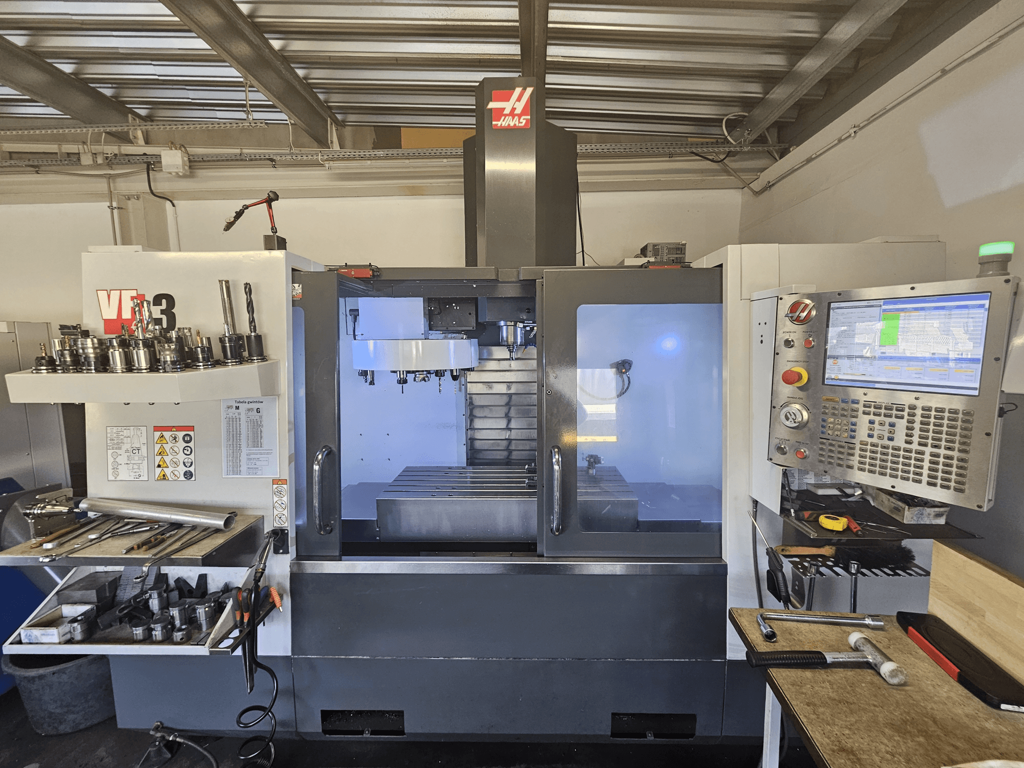 Haas VF-3 CNC-maskin i en verkstad, vy framifrån med verktyg, reglage och fräsområde med upplyst interiör.