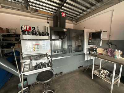 Haas VF-3 CNC-maskin i verkstad, framifrån med verktyg och reglage på intilliggande bord, med visning av tekniskt gränssnitt och säkerhetsinformation.