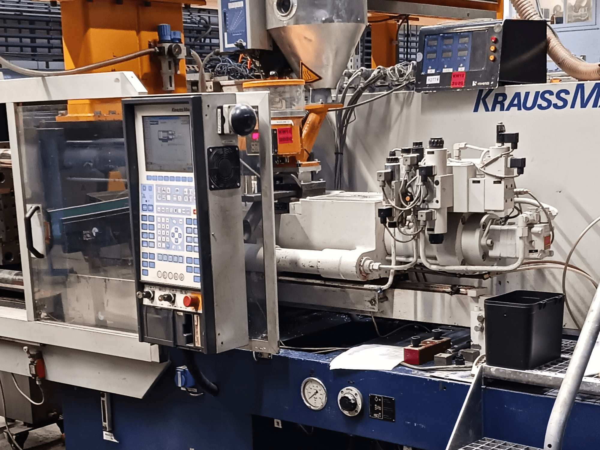 KraussMaffei formsprutningsmaskin med kontrollpanel, hydraulaggregat och verktyg i förgrunden, vy framifrån.