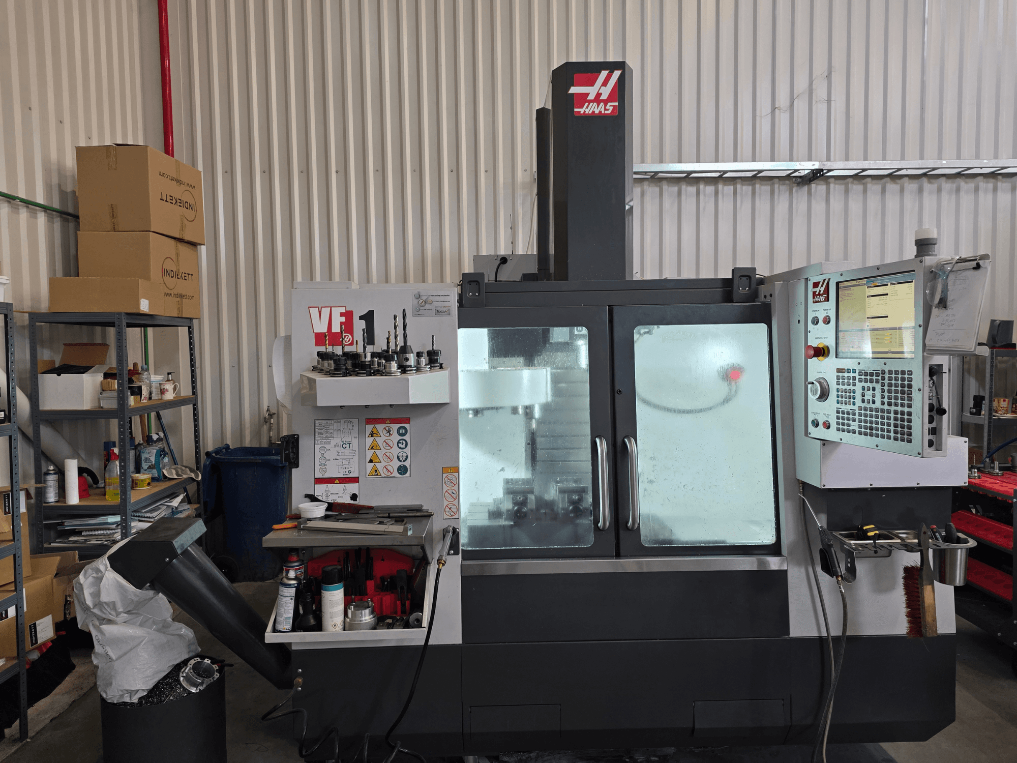 HAAS VF 1 vertikal fleroperationsmaskin i en verkstad, framifrån med kontrollpanel och fräsområde med verktyg.