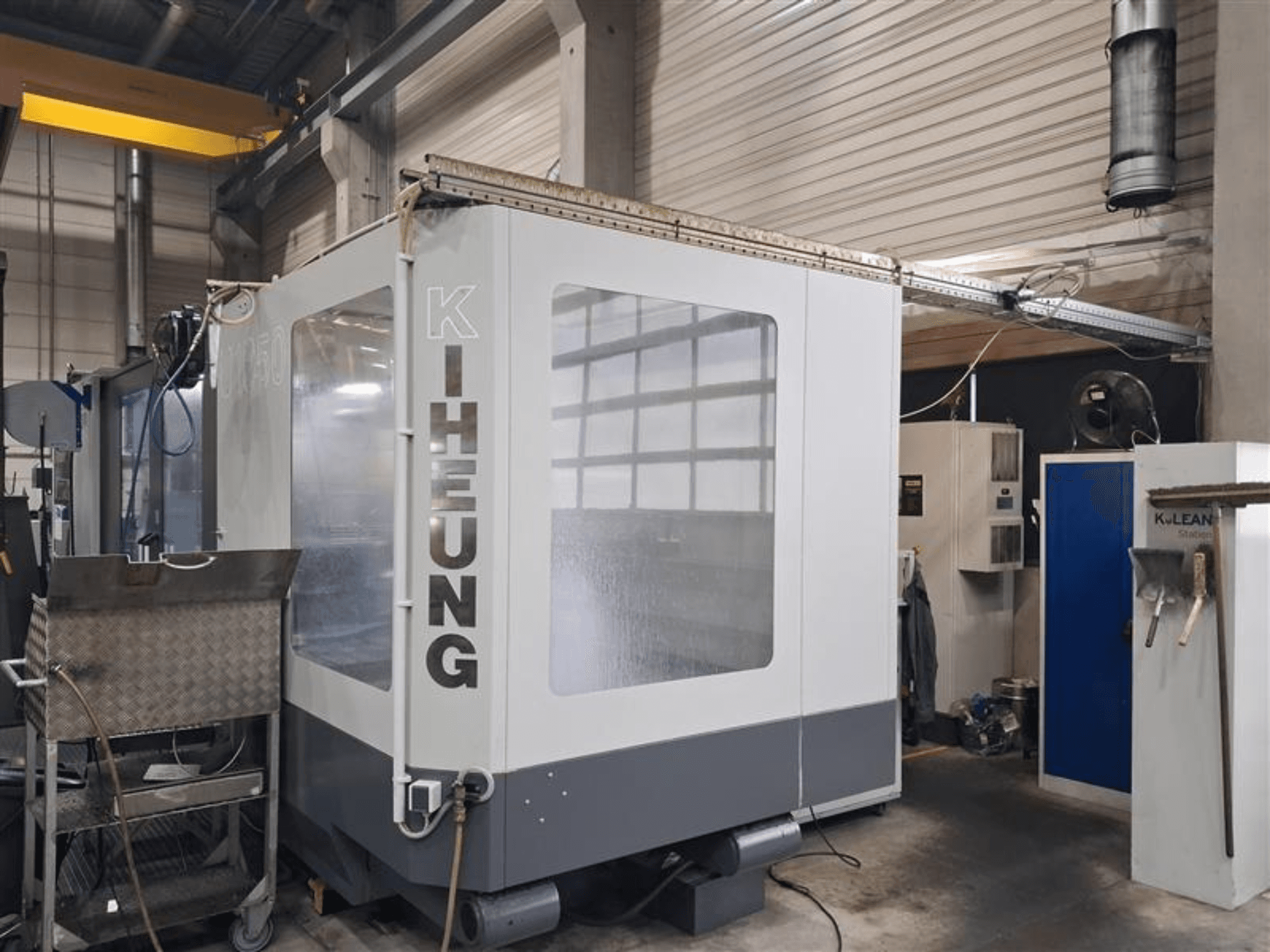 Fräsmaskin av sängtyp KIHEUNG Volmatec KNC U1050, framifrån sett med metallhölje och styrenhet i bakgrunden.