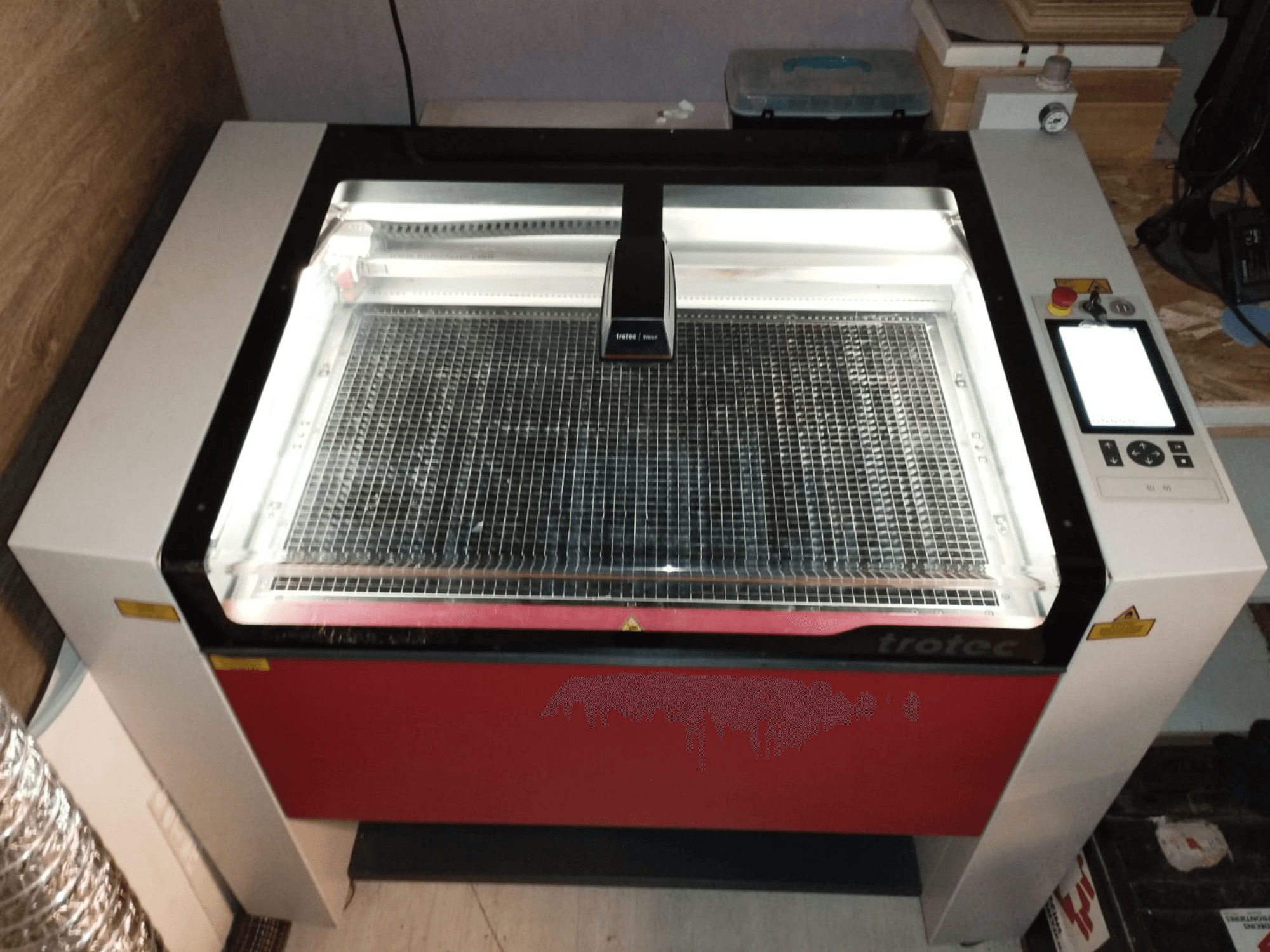 Trotec laserskärare med transparent lock, rasterbädd och kontrollpanel till höger; framifrån visar design och funktioner.