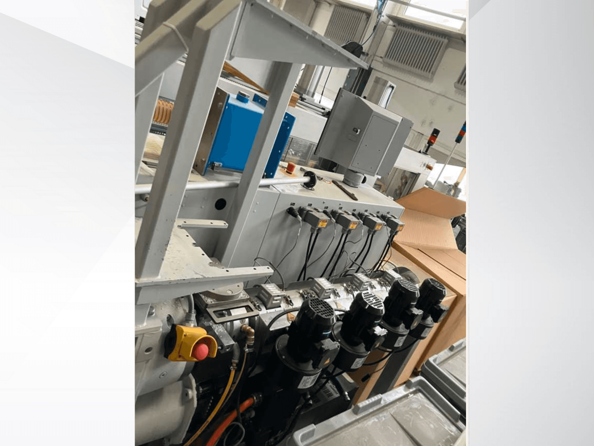 Kontrollpanel för industrimaskiner med flera motorer, mätare och en bildskärm; sidovy i en fabriksmiljö.