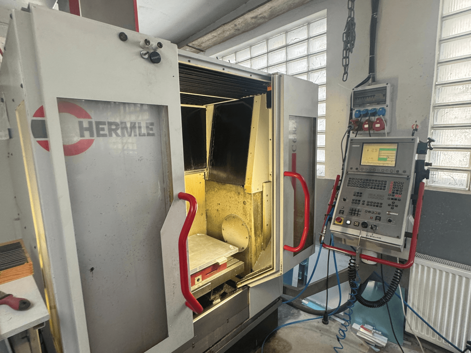 HERMLE C600V vertikal fleroperationsmaskin, framifrån med öppen dörr, kontrollpanel och invändigt arbetsområde.
