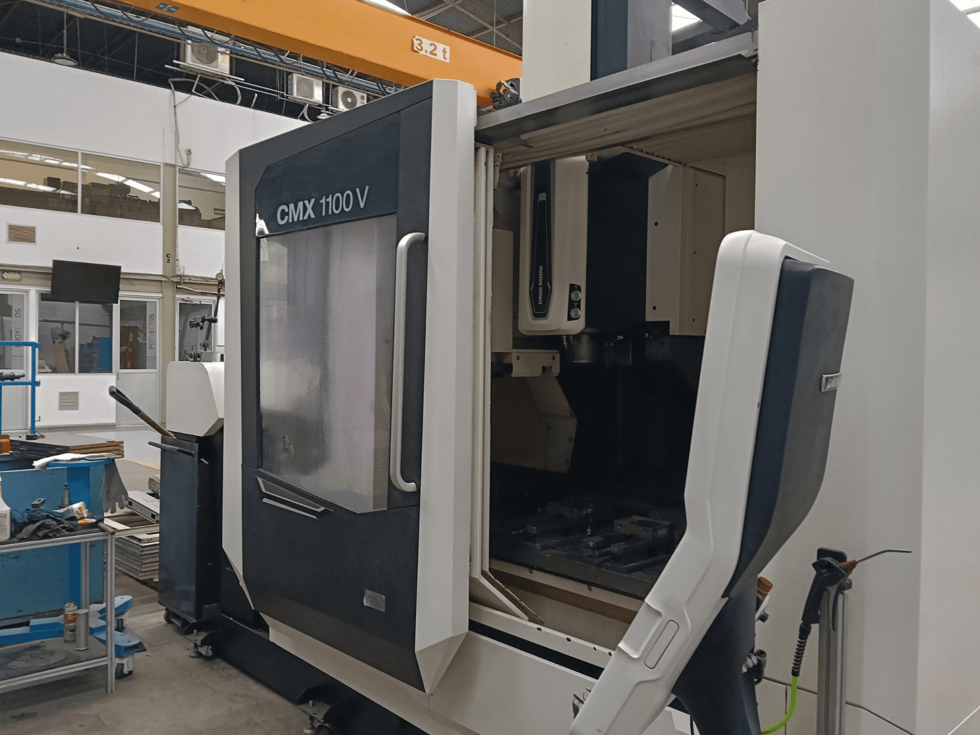 Vertikalt bearbetningscenter DMG MORI CMX 1100 V, framifrån sett med öppen lucka och verktygsinställning inuti i en industrilokal.
