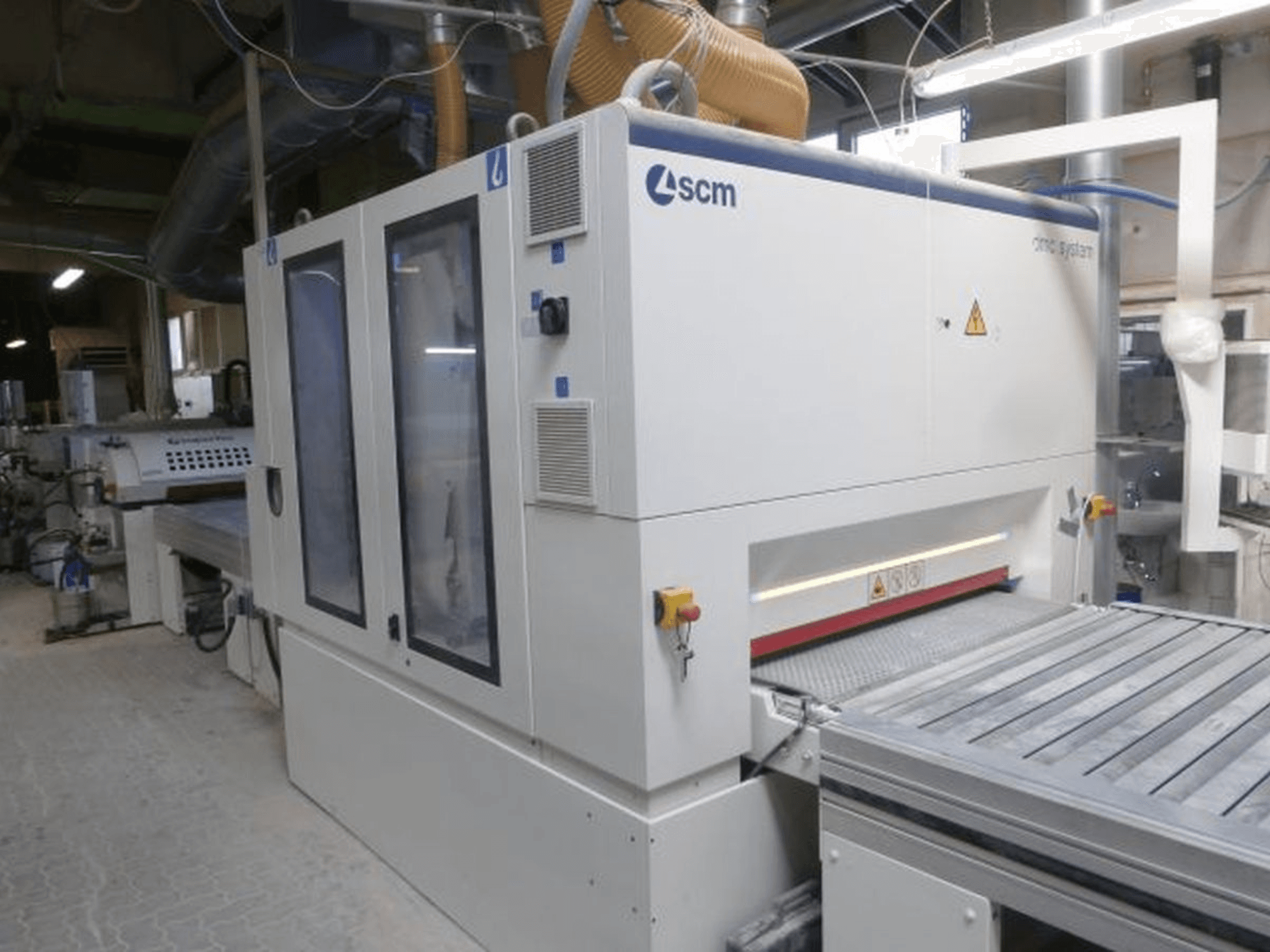 Bandslipmaskin SCM DMC SY TC 1350 i en verkstad, sidovy som visar kontrollpanelen och slipytan med säkerhetsfunktioner.