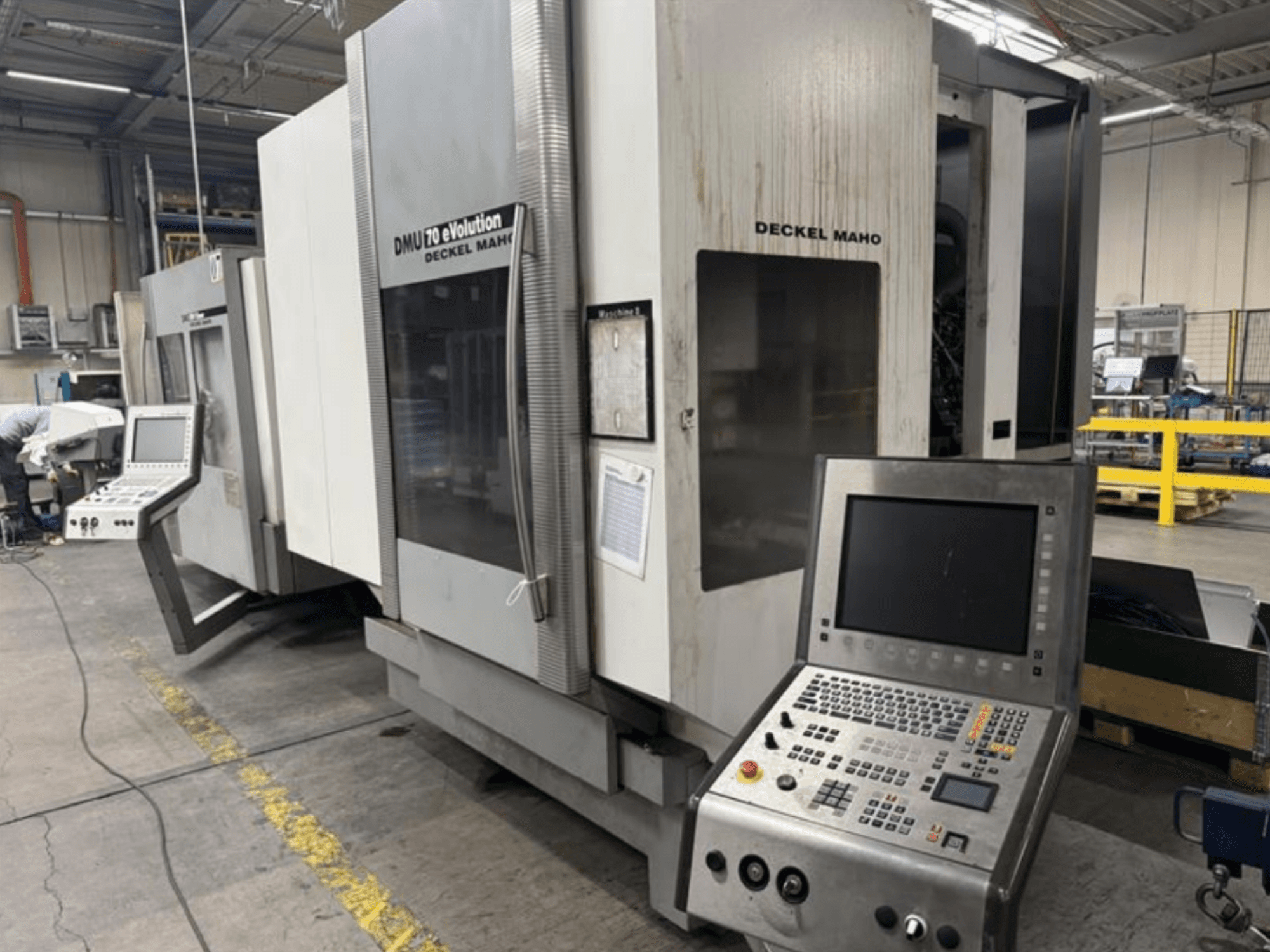 Frontvy av en Deckel Maho DMU 70 eVOLUTION CNC-maskin med kontrollpanel, placerad i en tillverkningsanläggning.