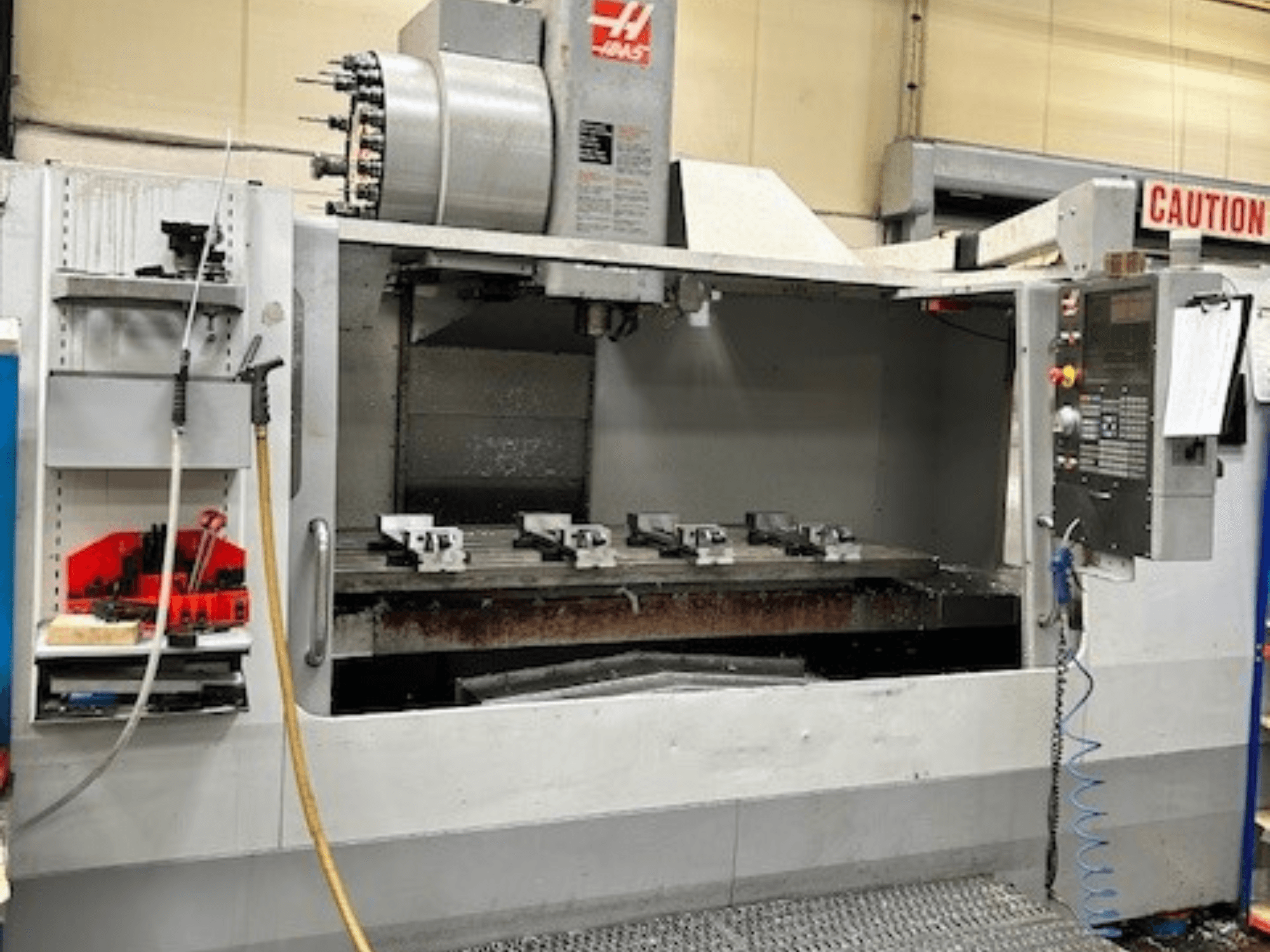 HAAS VF-9/40HE vertikal fleroperationsmaskin, vy framifrån, med verktygshållare och tillbehör synliga på sidan.