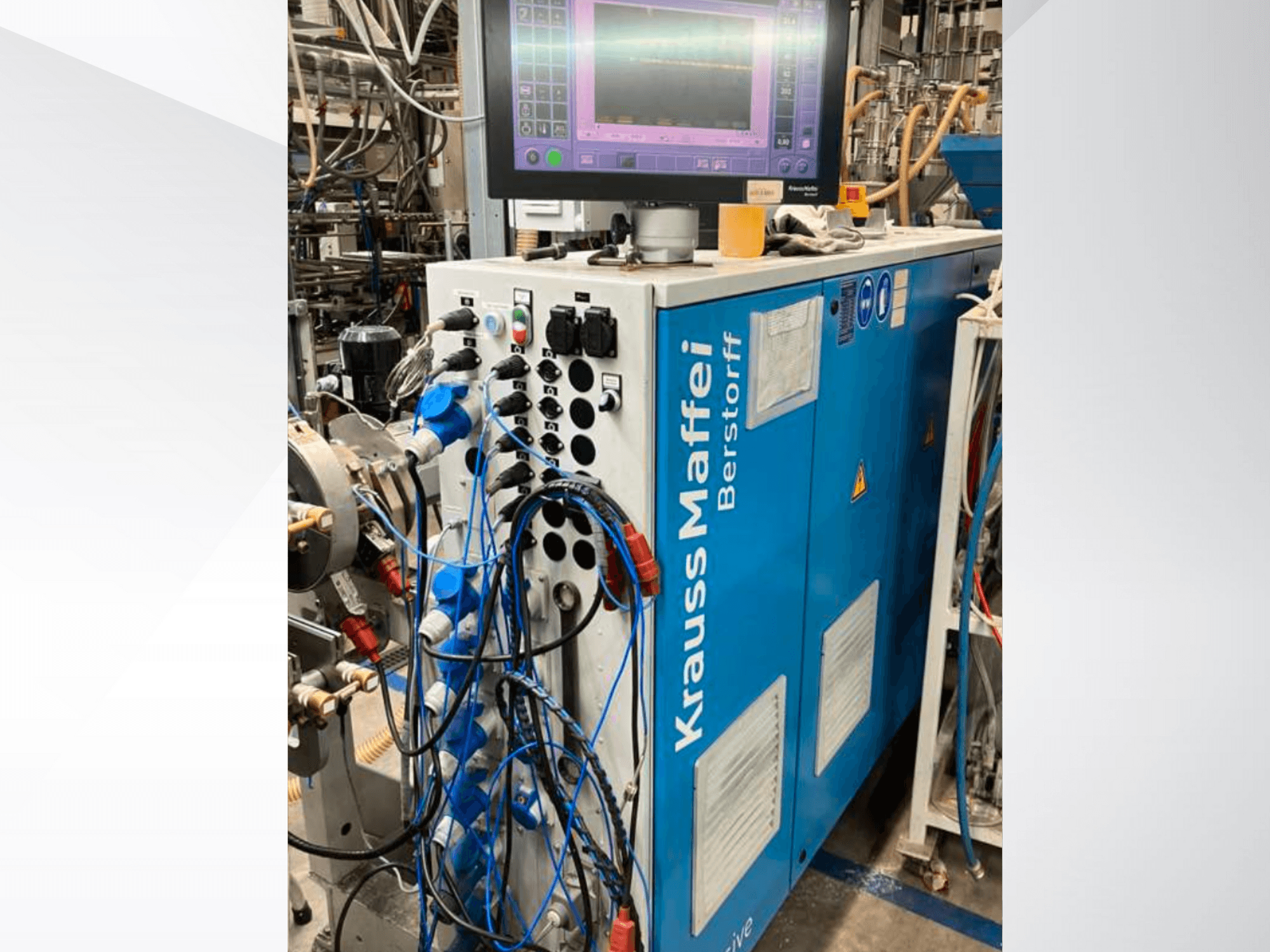 Krauss Maffei Berstorff industrimaskin med kontrollpanel och monitor, med olika knappar och anslutna slangar, vy från sidan.