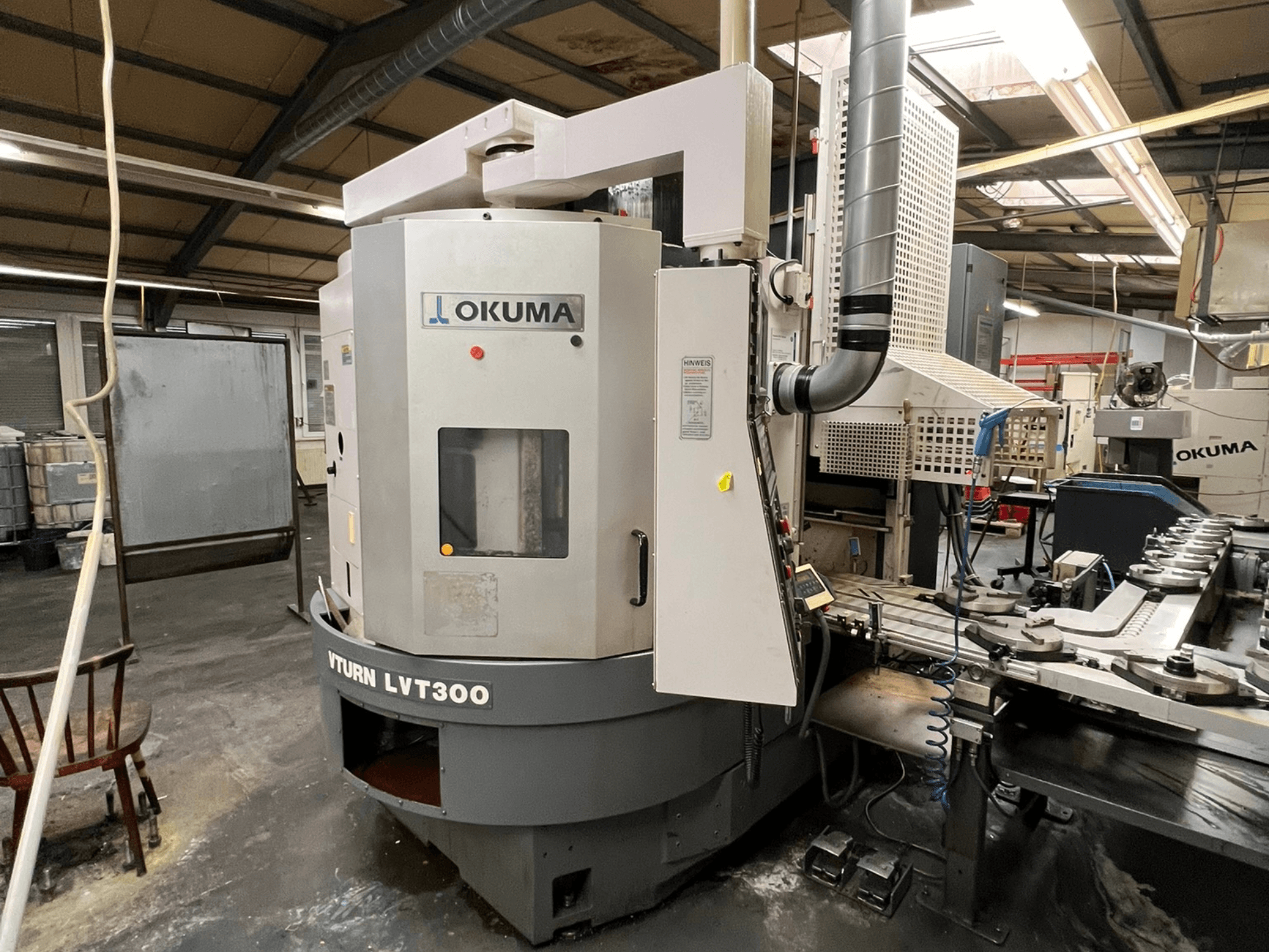 Okuma Vturn LVT300 CNC-svarv, sidovy i industriell miljö, visar kontrollpanel och kylsystem.
