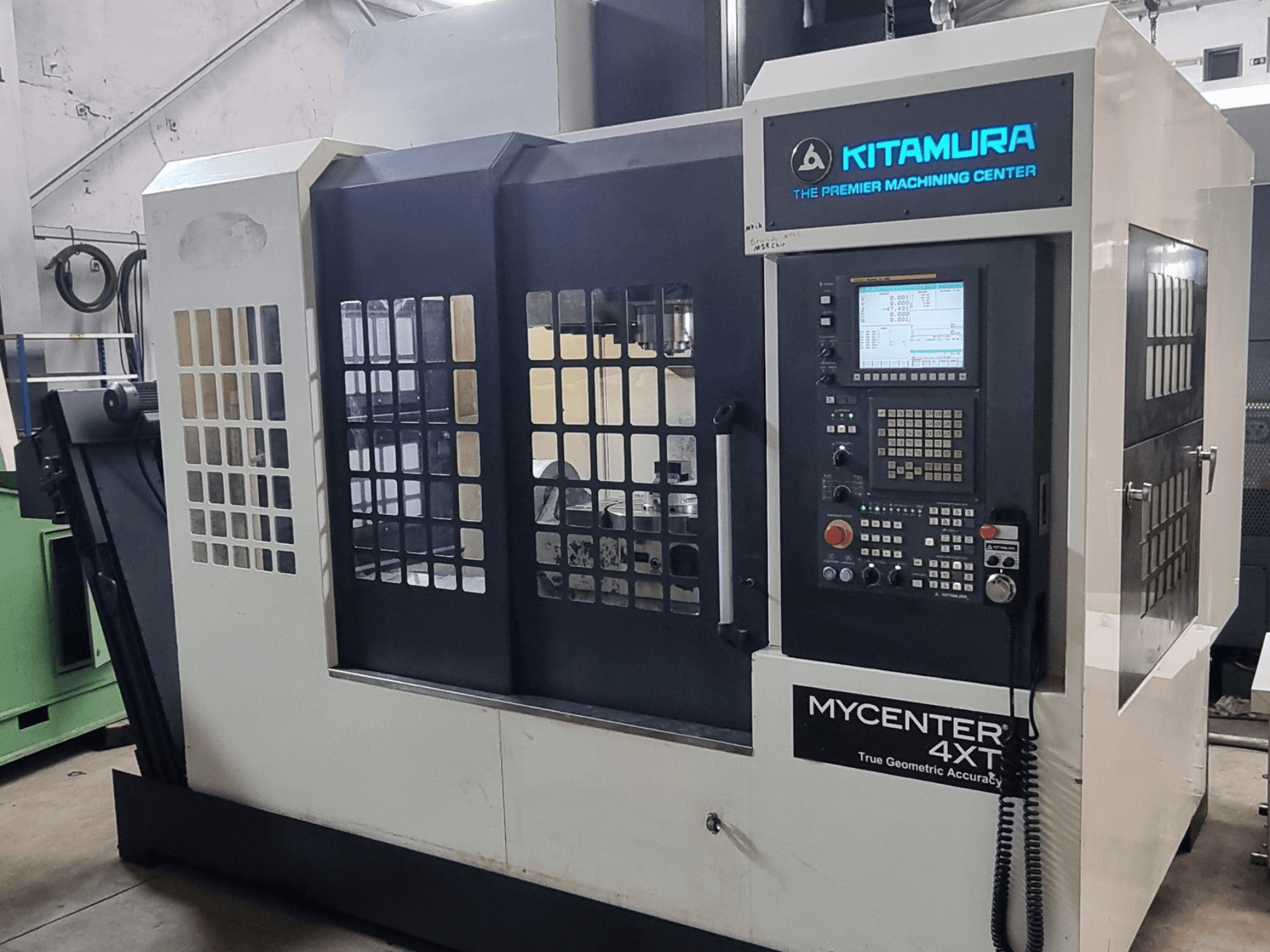 Alternativtext: Kitamura MYCENTER 4XT vertikalt bearbetningscenter, framifrån, där kontrollpanelen och maskinens detaljer visas i en verkstadsmiljö.