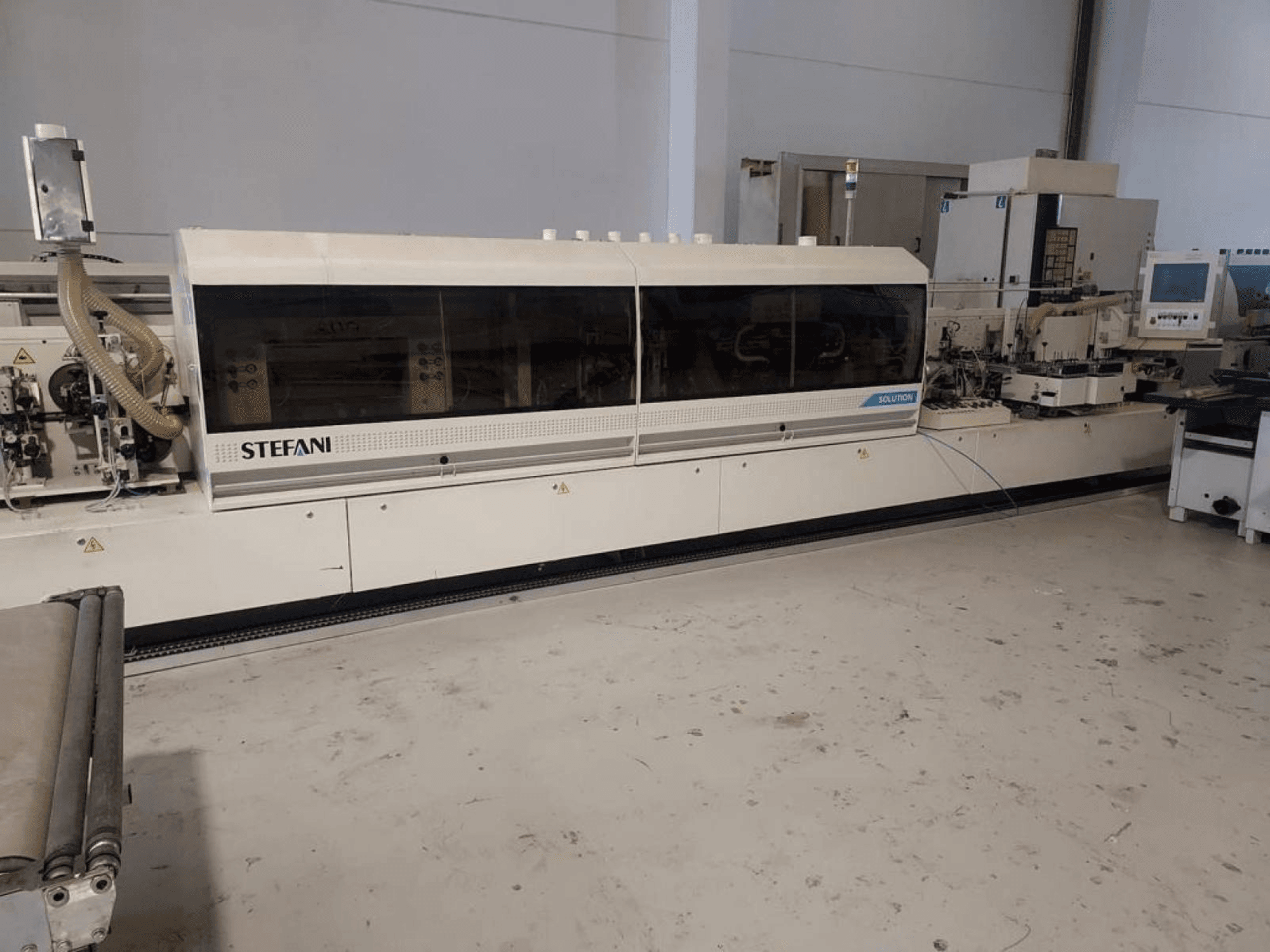 Stefani Solutions kantlistningsmaskin, framifrån, med dammutsugningssystem och kontrollpanel synliga, i en verkstadsmiljö.