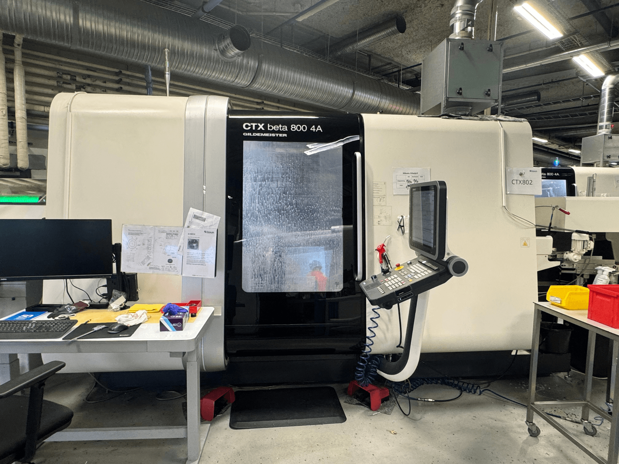 CTX beta 800 4A CNC-maskin i en verkstad, sidovy som visar kontrollpanel och arbetsyta belamrad med verktyg och dokument.