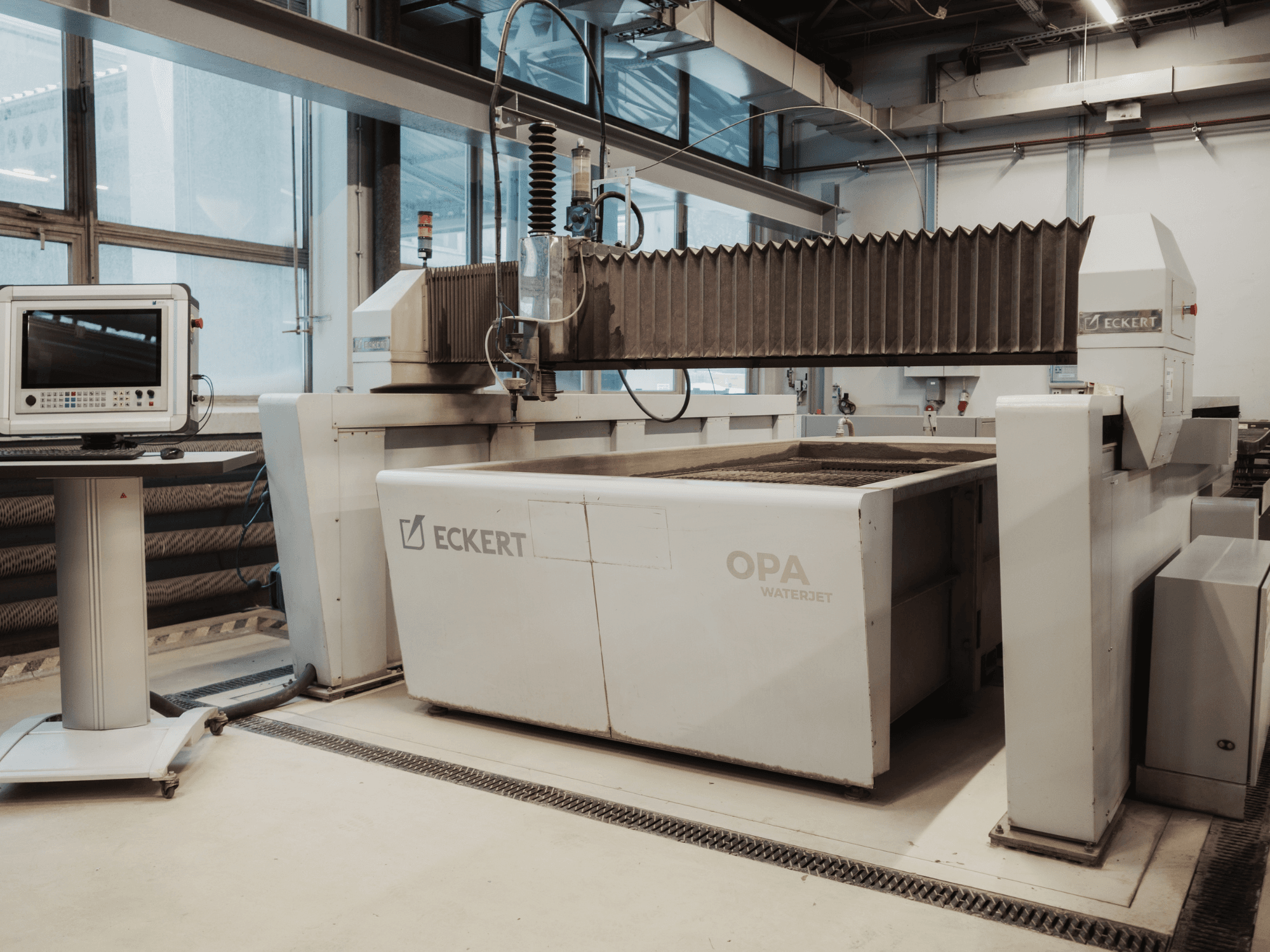 En ECKERT OPAL-vattenstråleskärmaskin i en verkstad, sedd framifrån med kontrollpanelen intill.