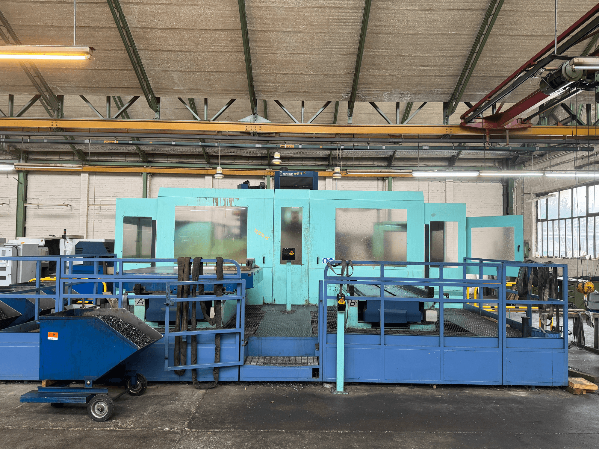 Industriell blå CNC-maskin med skyddspaneler, framifrån, med verktygsförvaring och en avfallsvagn på sidan.