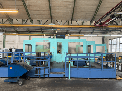 Industriell blå CNC-maskin med skyddspaneler, framifrån, med verktygsförvaring och en avfallsvagn på sidan.