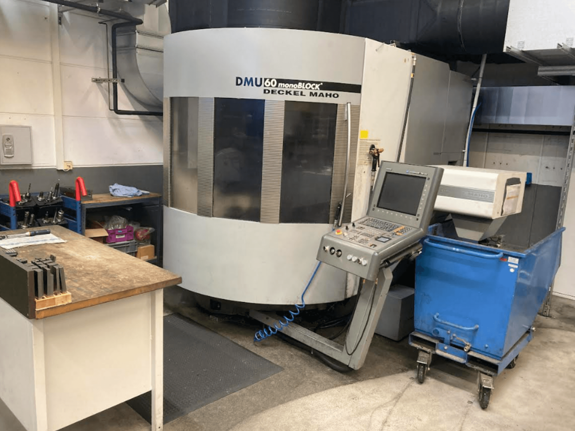 DMG MORI DMU 60 Monoblock vertikalt bearbetningscenter, framifrån med kontrollpanel, arbetsyta och blå verktygsvagn synliga.
