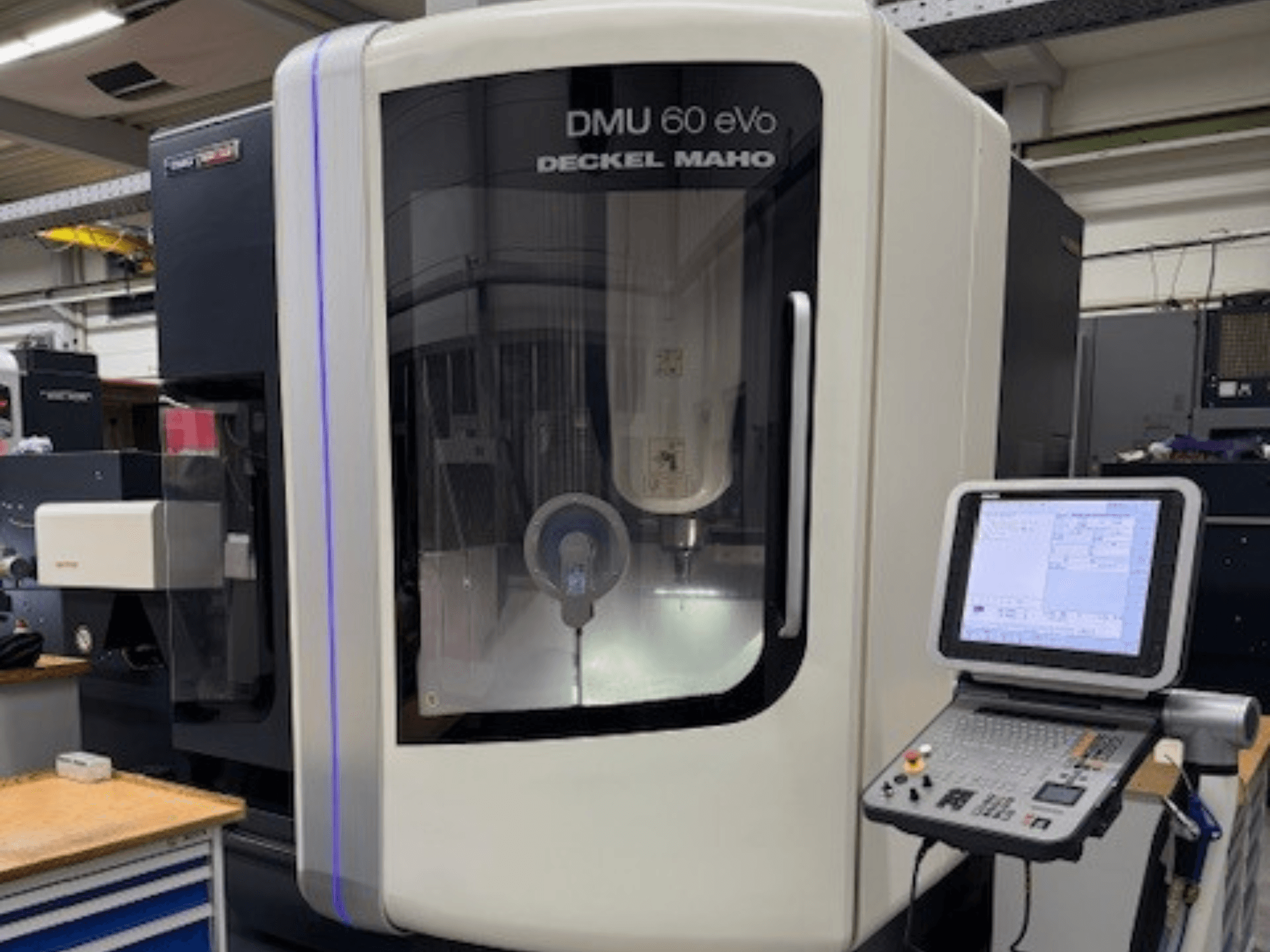 DMU 60 eVo by DECKEL MAHO, CNC-fräsmaskin framifrån med kontrollpanel och displayskärm, visar precisionskomponenter.