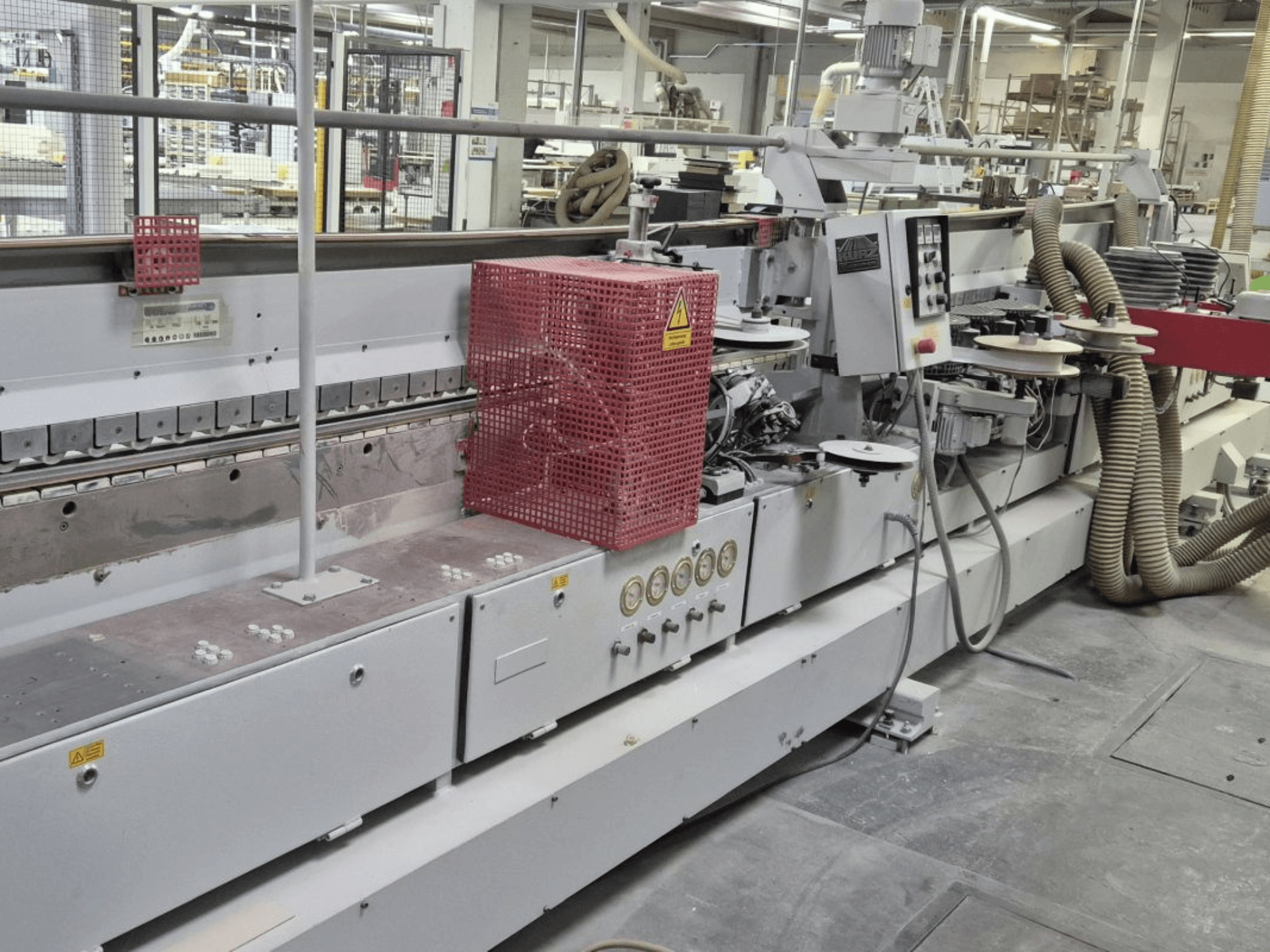 Kantlistningsmaskin med kontrollpanel, sugslangar och röd skyddshuv, sedd från sidan.