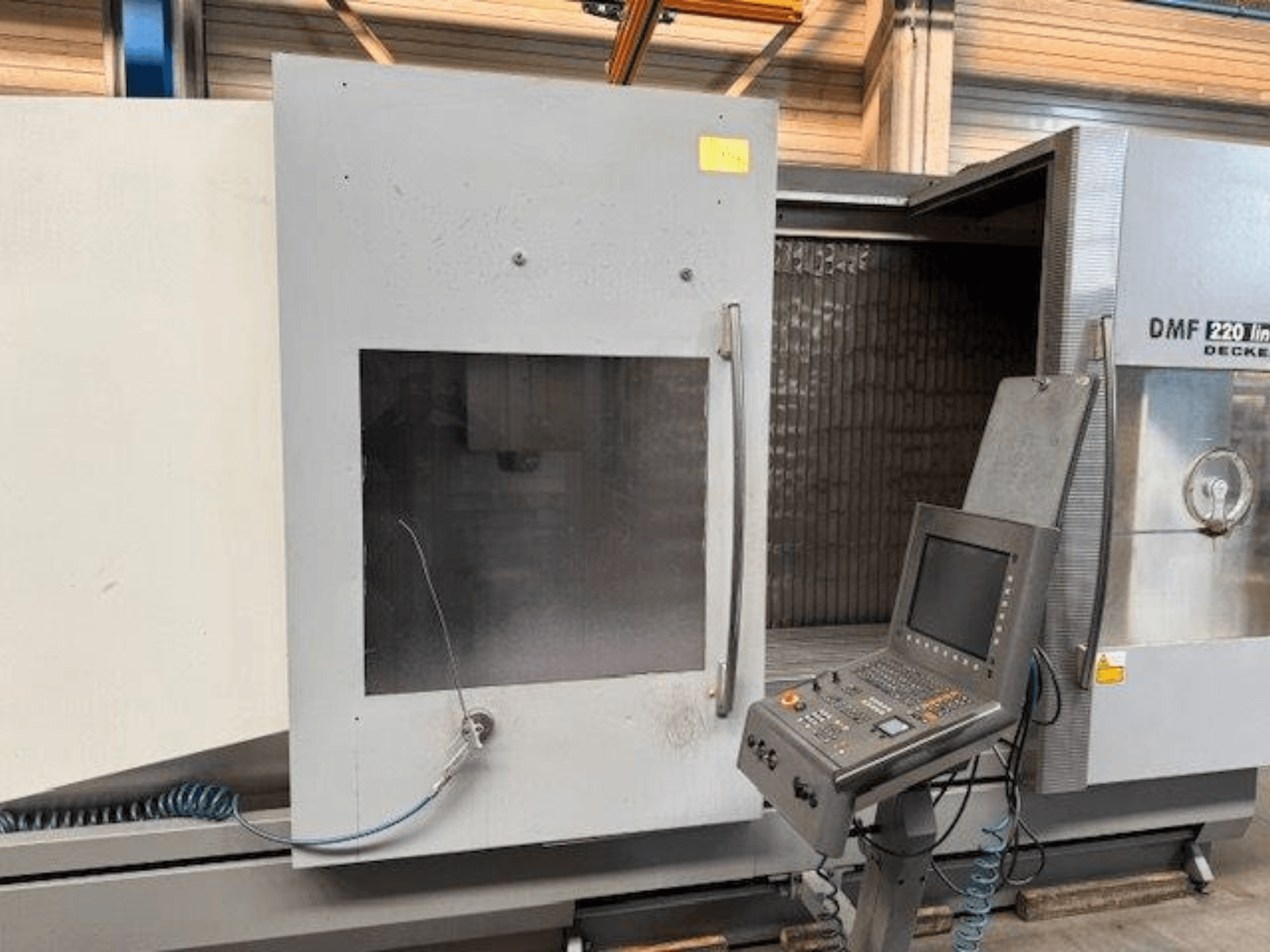 Frontvy av DECKEL MAHO DMF 220 Linear vertikalt bearbetningscenter, som visar kontrollpanelen och den öppna maskindörren.