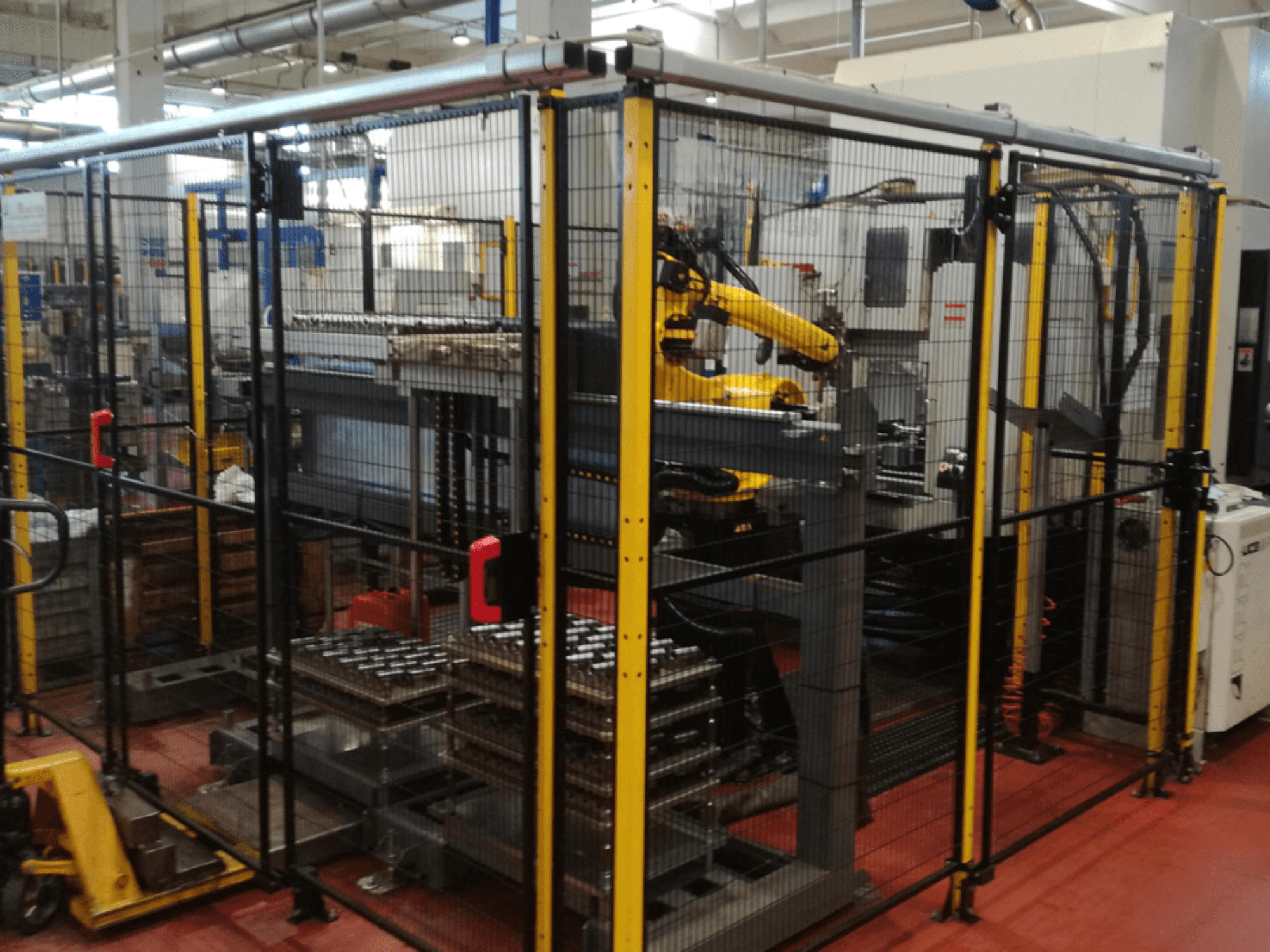 Enshu EV450 vertikal bearbetningscenter i ett inhägnat arbetsområde med robotarmar och flera staplade arbetsstycken. Vy framifrån.