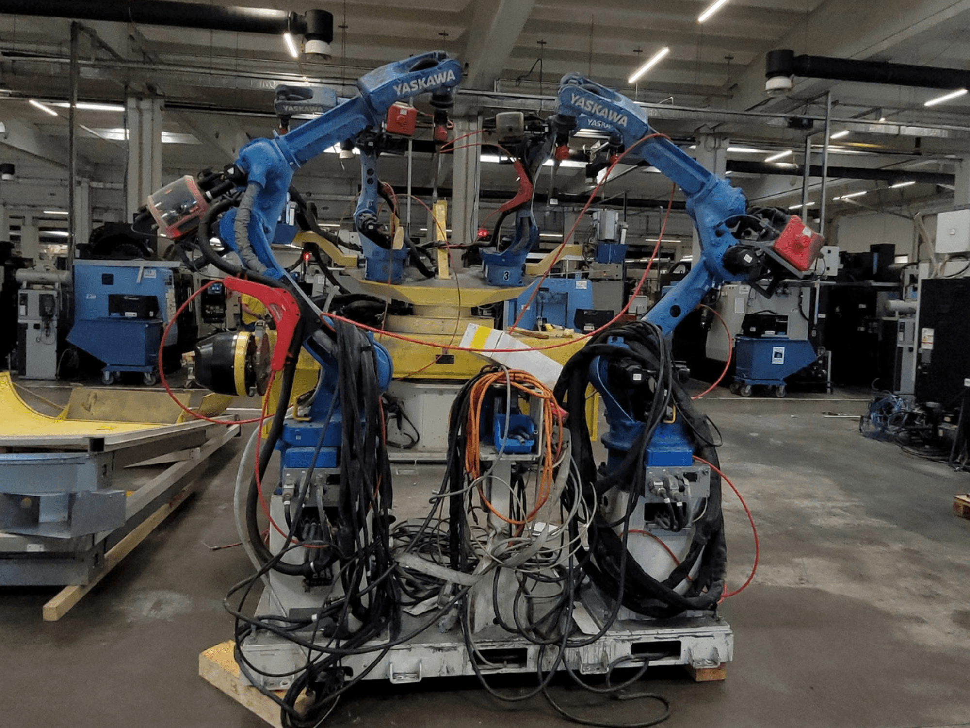 Yaskawa Robotic Welding Cell RWC L1_OS 15330, framifrån, med två blå robotar utrustade med omfattande kablage och svetsverktyg.