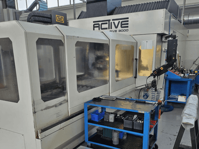 Aktiv 3000 CNC-maskin i en verkstad, framifrån med verktyg på en blå vagn, synliga kontroller och arbetsområde inuti.