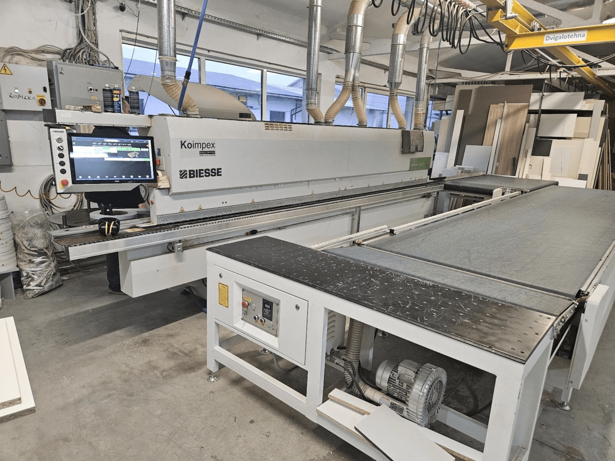 BIESSE Akron 1440 En kantlistmaskin i en verkstad, sidovy som visar kontrollpanel och transportband.