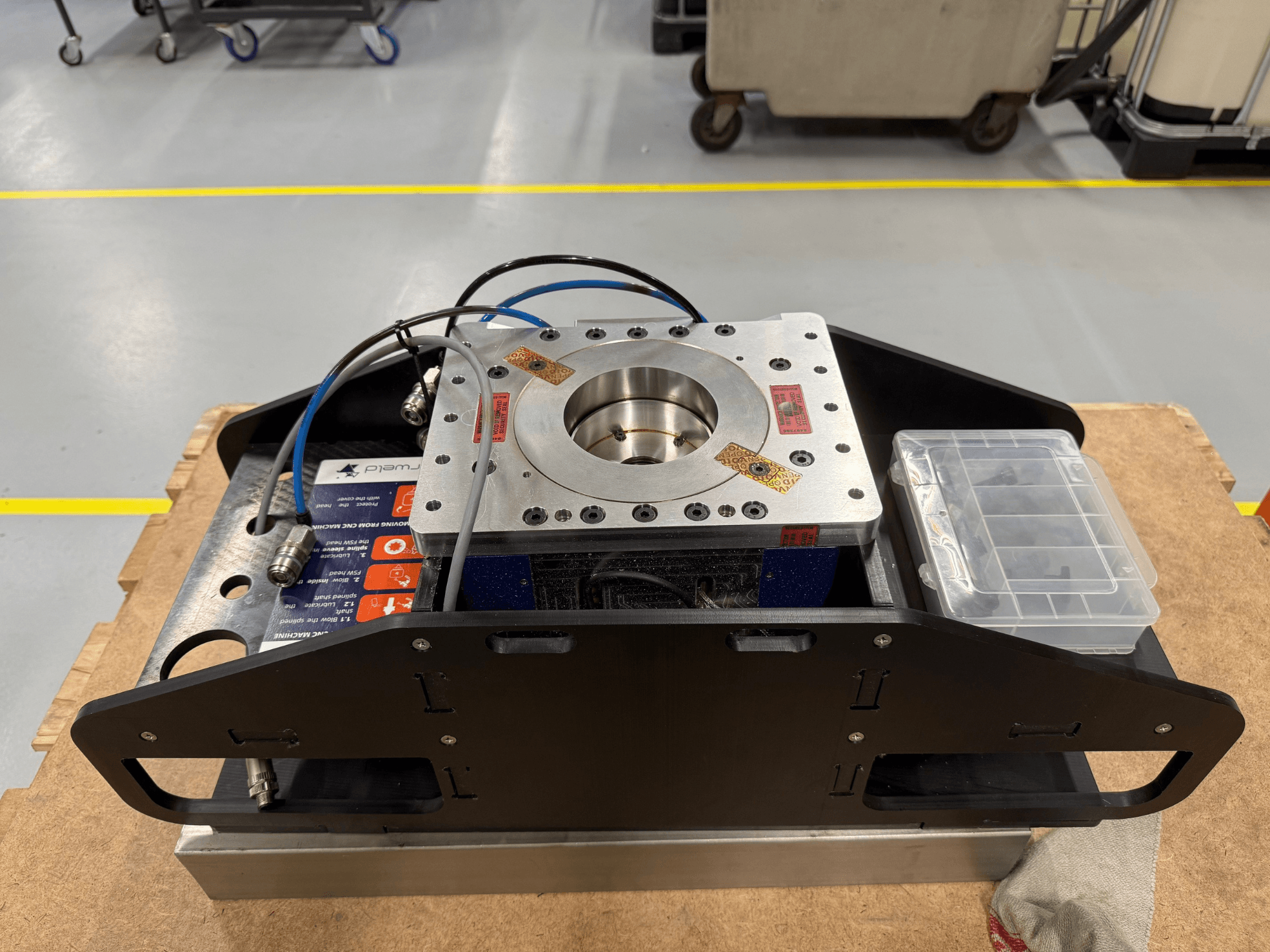 Maskinbearbetad metallkomponent med blå kablar, tillbehörsfodral och platt bas, visad uppifrån, idealisk för mekaniska applikationer.