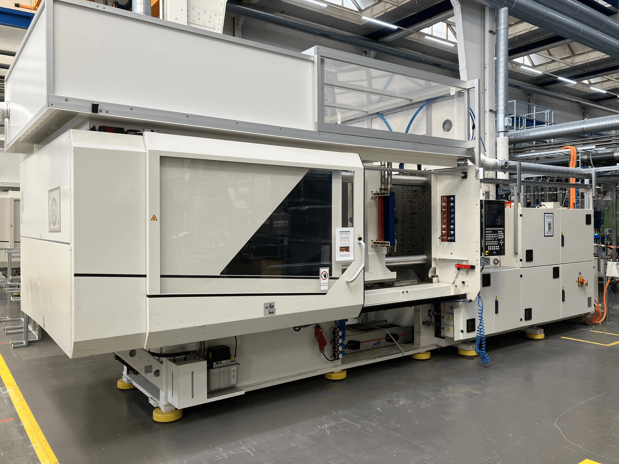 Sidovy av en formsprutningsmaskin, modell AET, med kontrollpanel och genomskinliga luckor, i en industrimiljö.