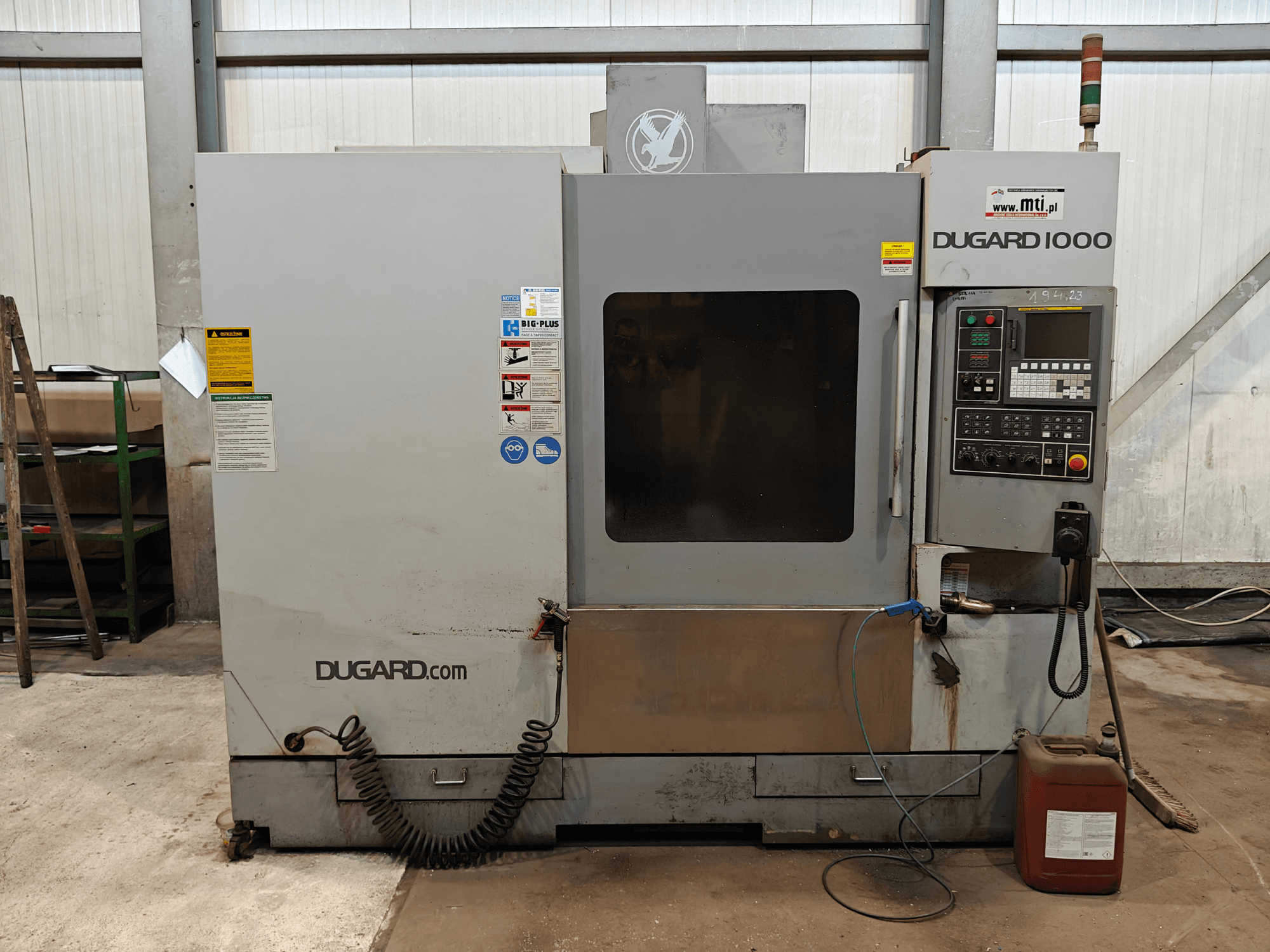 Dugard 1000 CNC-maskin, framifrån, med kontrollpanel, säkerhetsetiketter och oljebehållare, i en verkstadsmiljö.